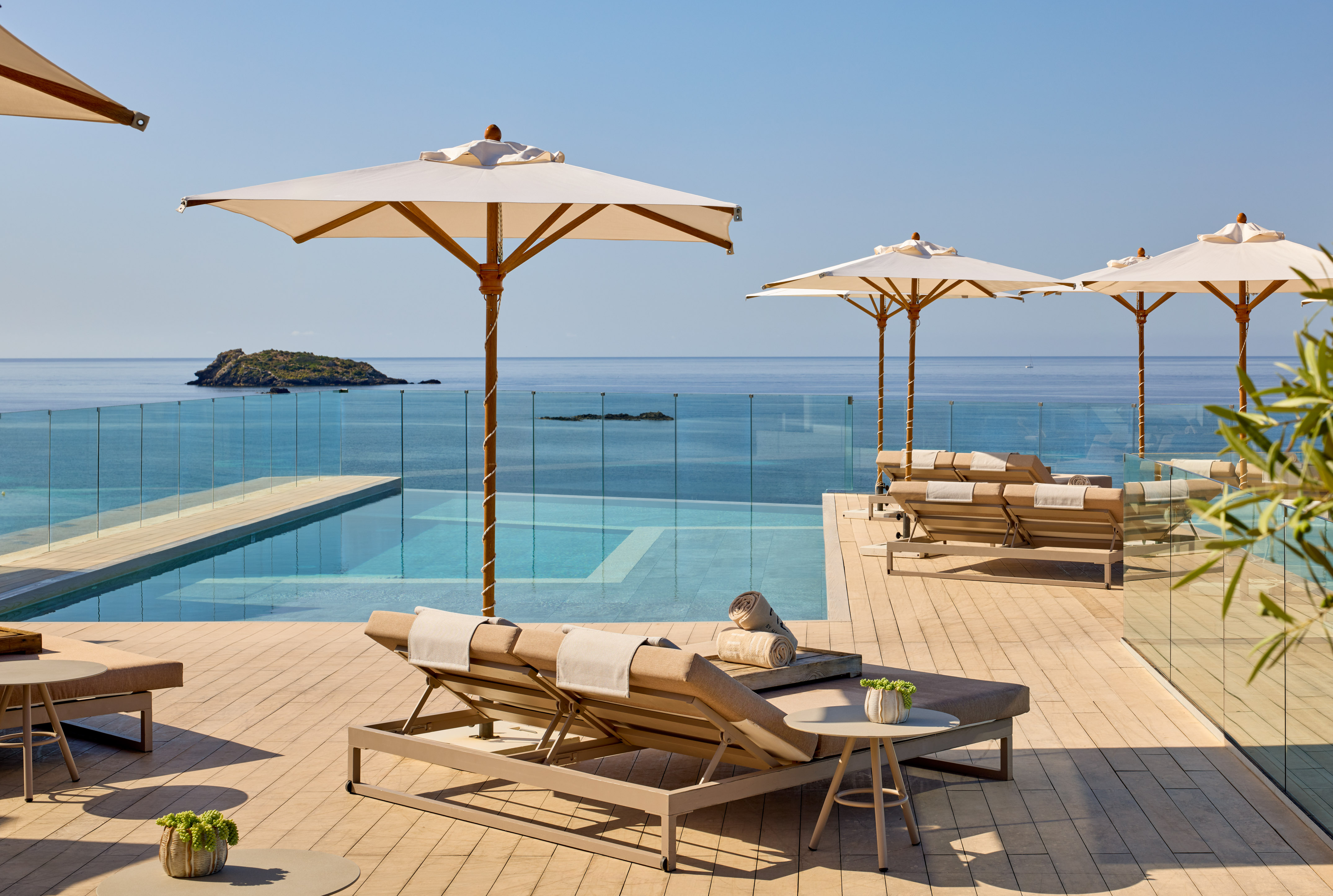 Luxury hotel infinity pool overlooking ocean, sun loungers, and umbrellas.