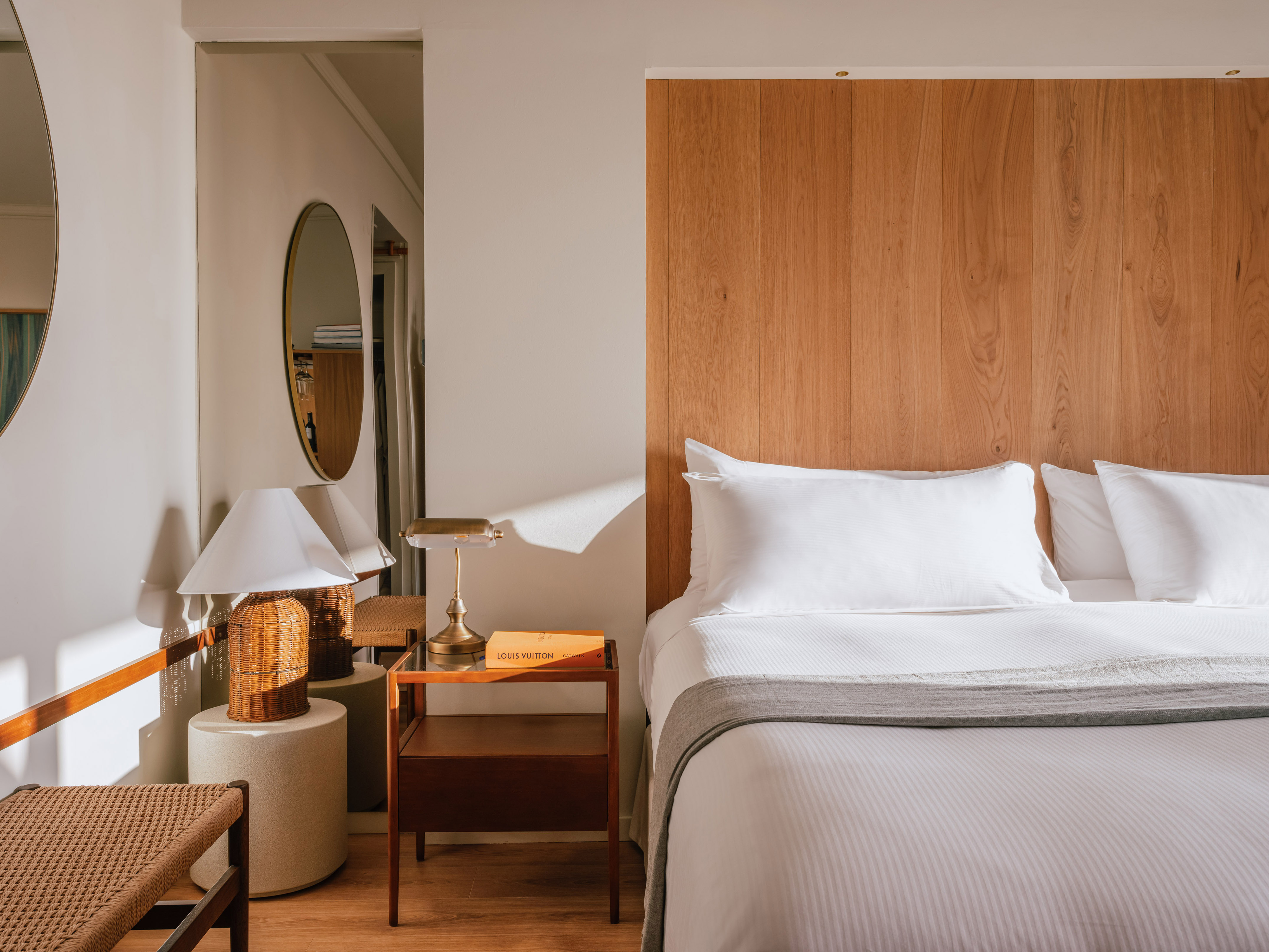 Modern hotel bedroom with wooden headboard, white bedding, and sleek nightstand.