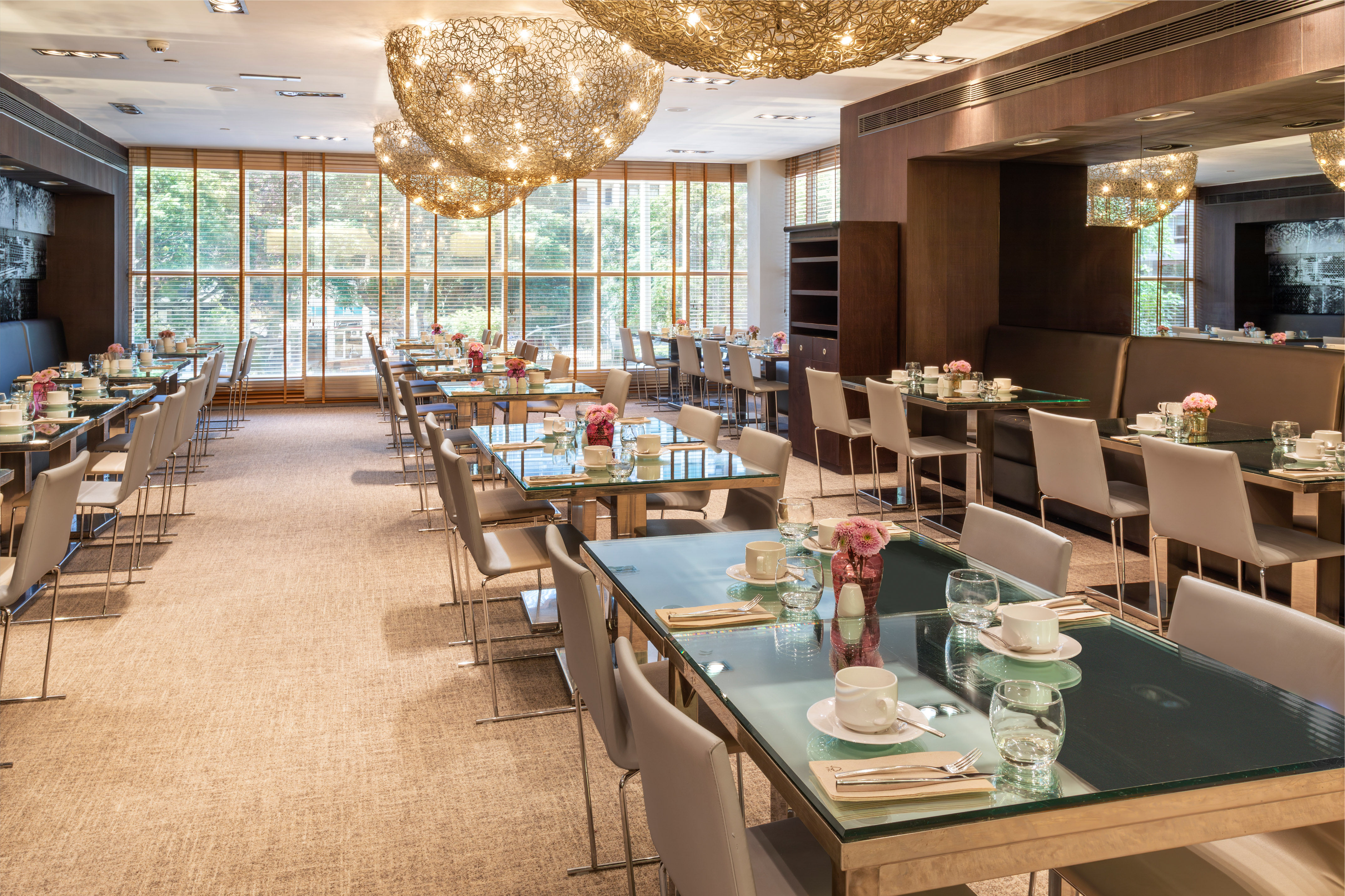 Modern dining room with glass tables, light chairs, and decorative chandeliers.