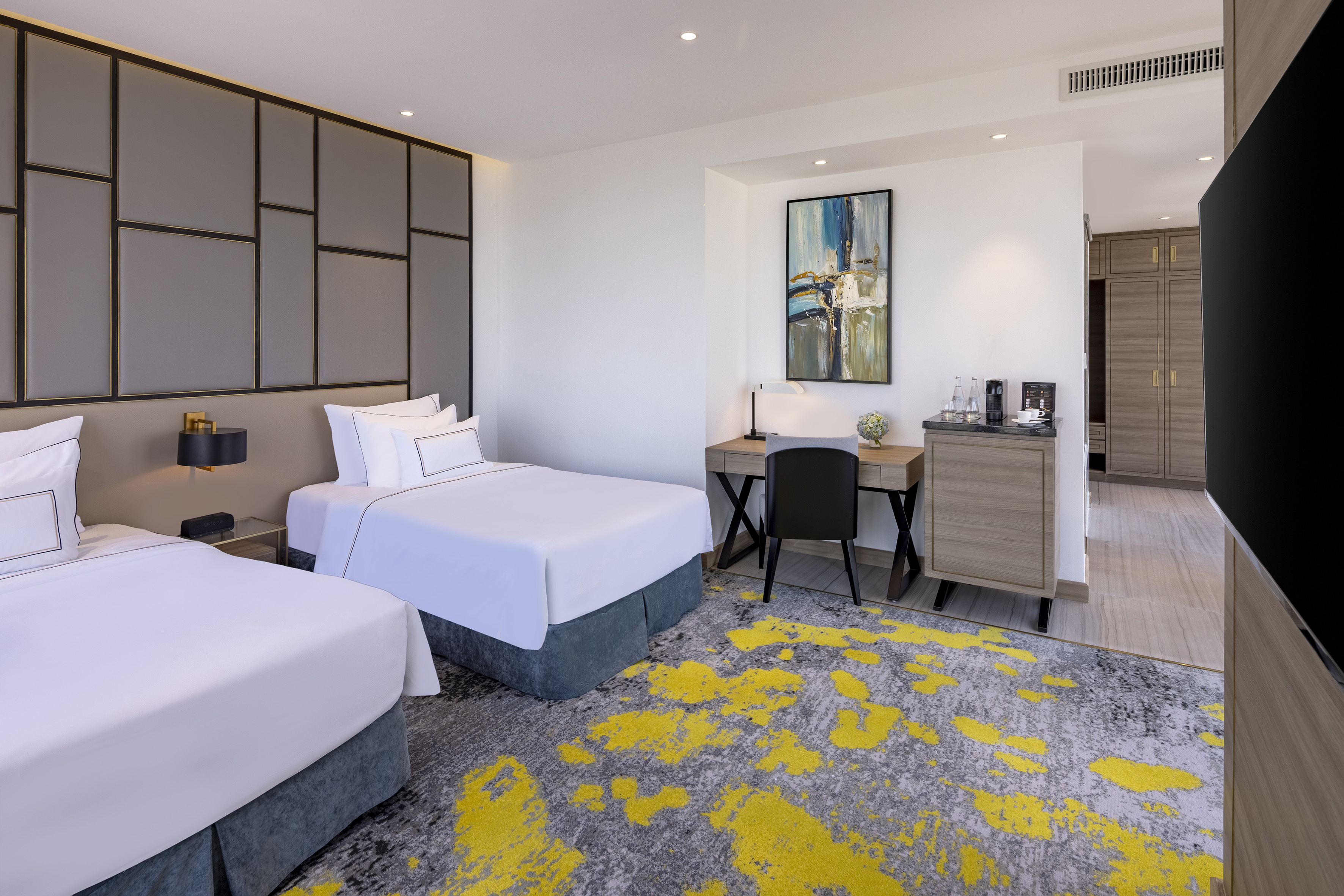 Modern twin hotel room with desk, minibar, and striking grey-yellow carpet.