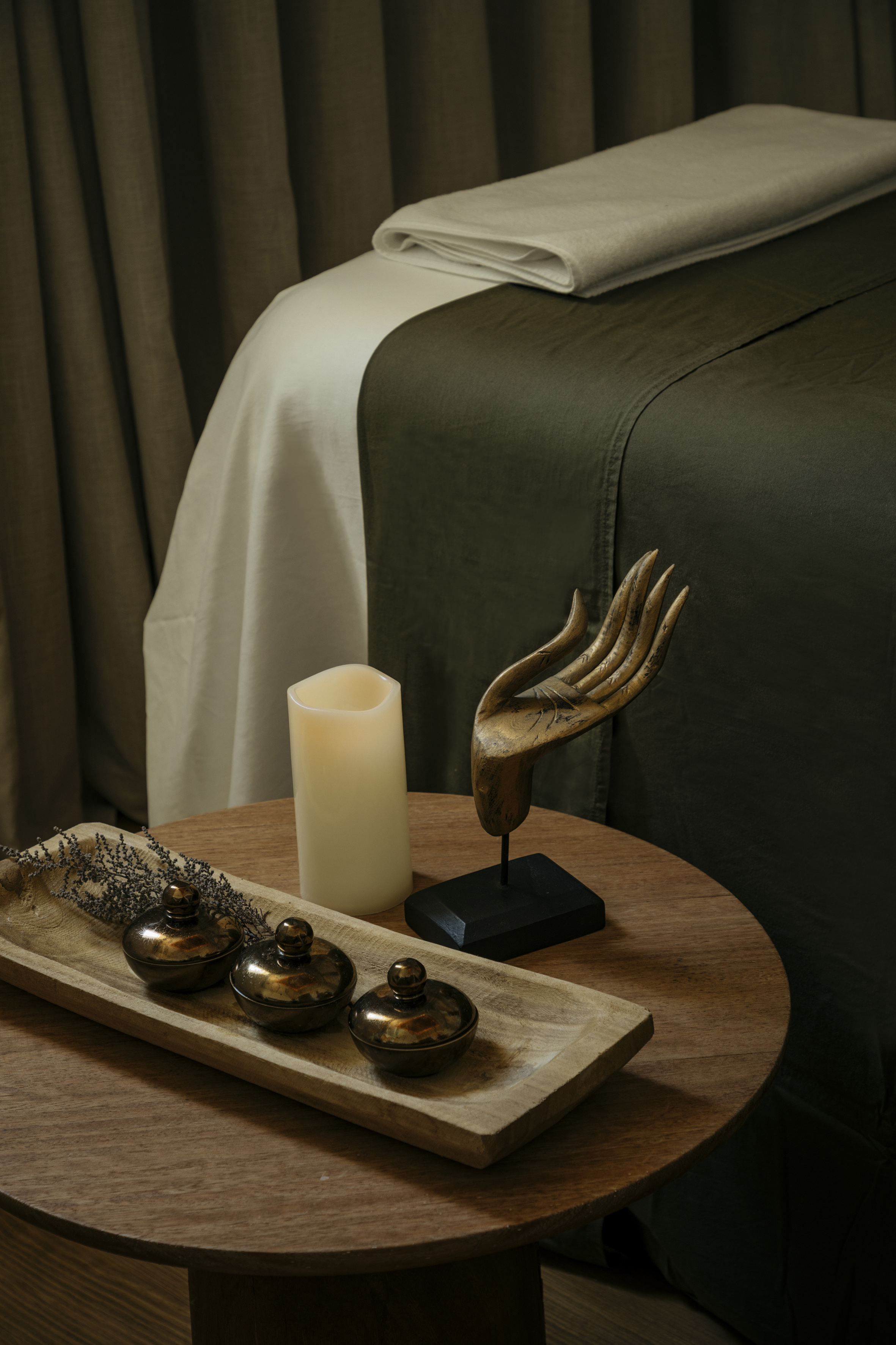 Spa massage table with olive green sheets, candle, and wooden hand decor.