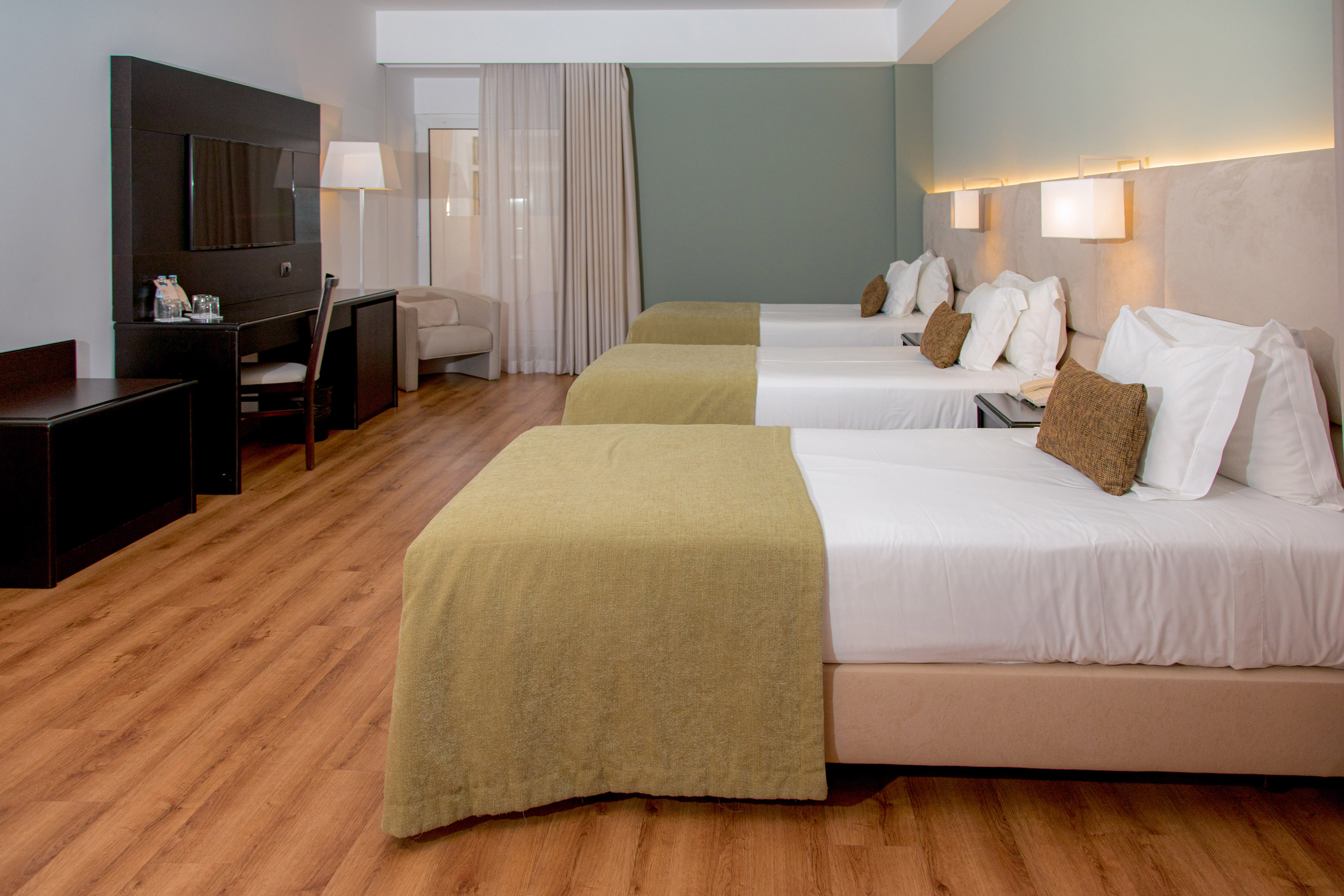 Triple hotel room with three single beds, desk, TV, and modern decor.