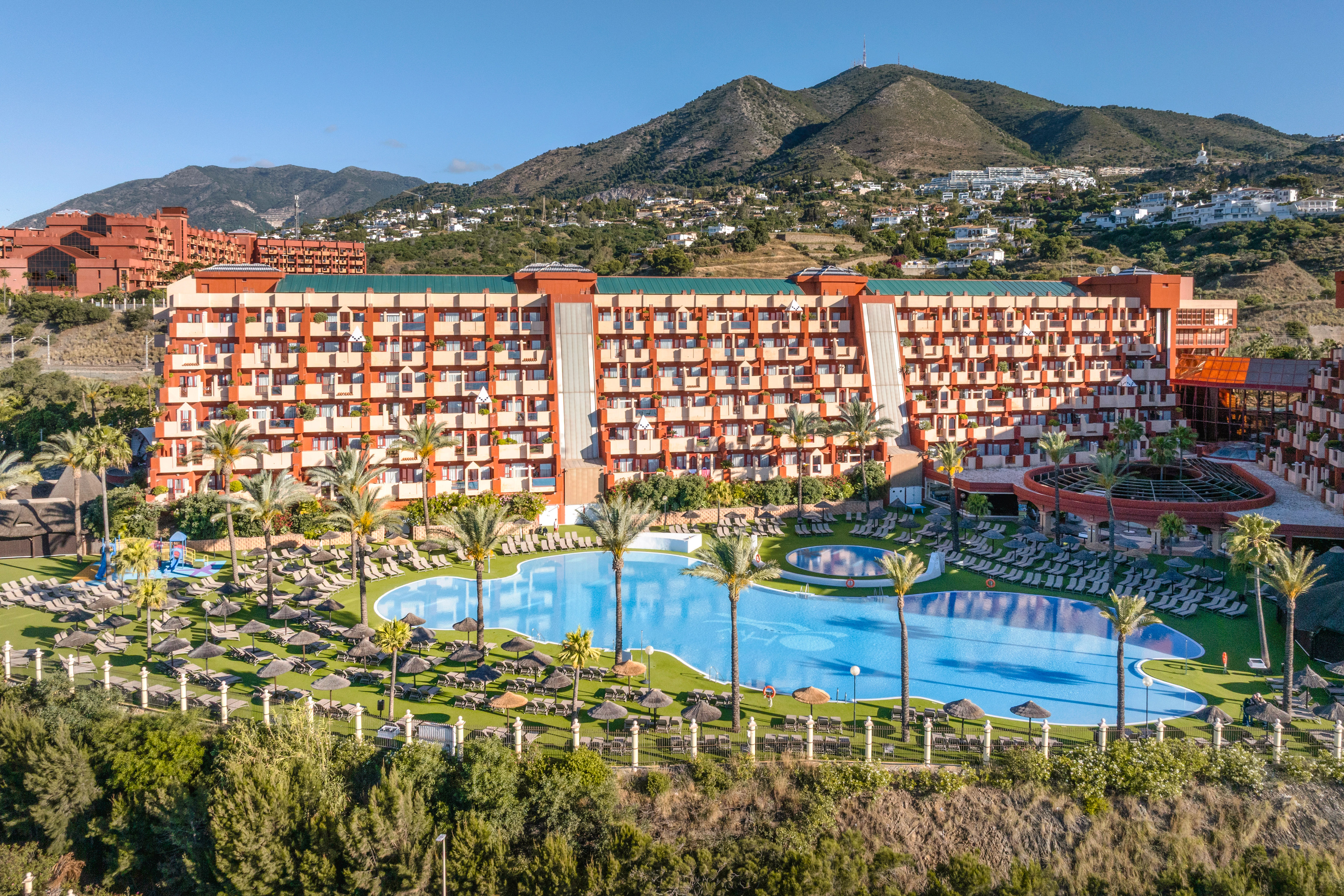 Resort costero con piscina, palmeras y edificios escalonados frente al mar.