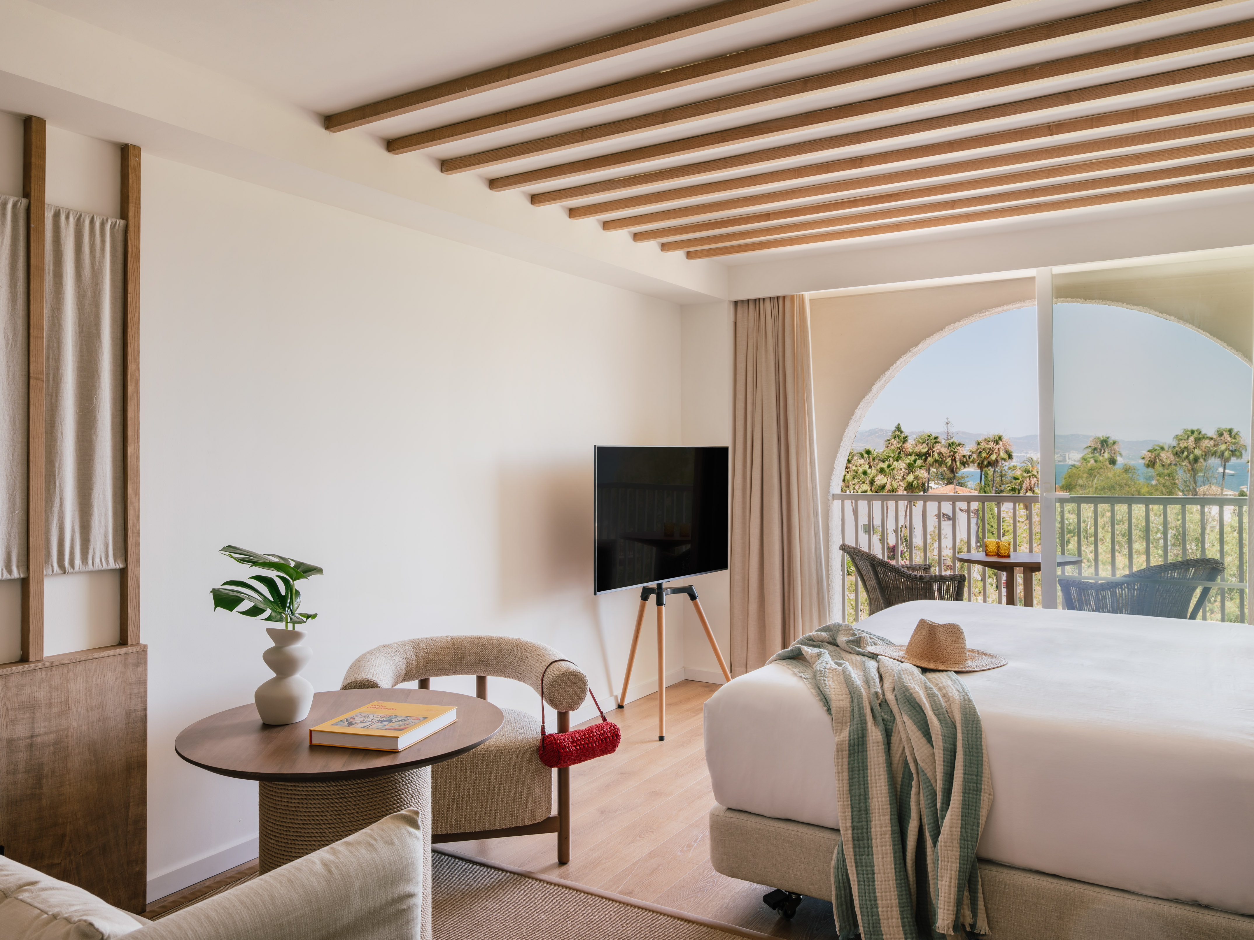 Modern resort room with sea view balcony, bed, TV, and natural wood accents.