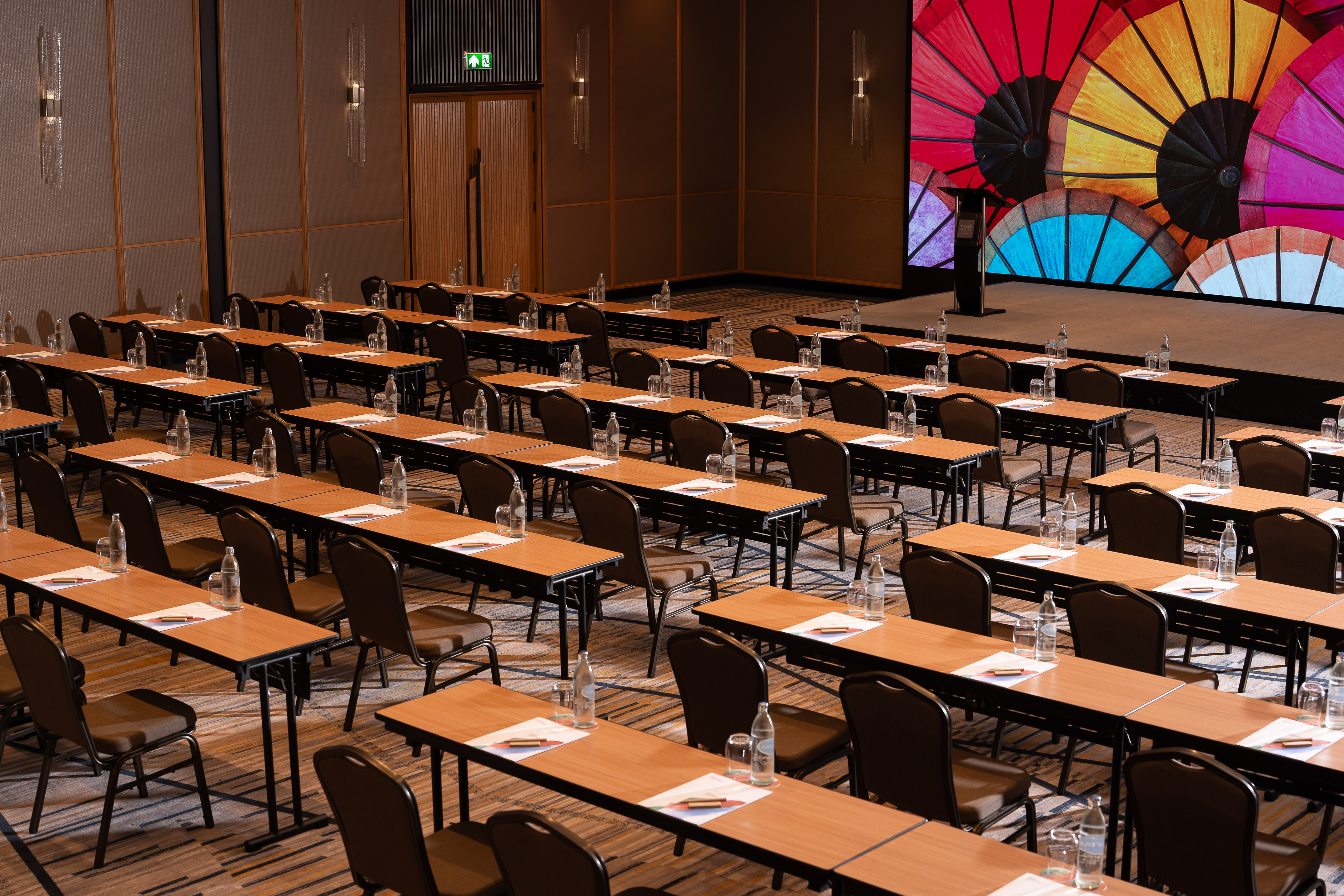 Conference room prepared for meeting with tables, chairs, and large colorful screen.