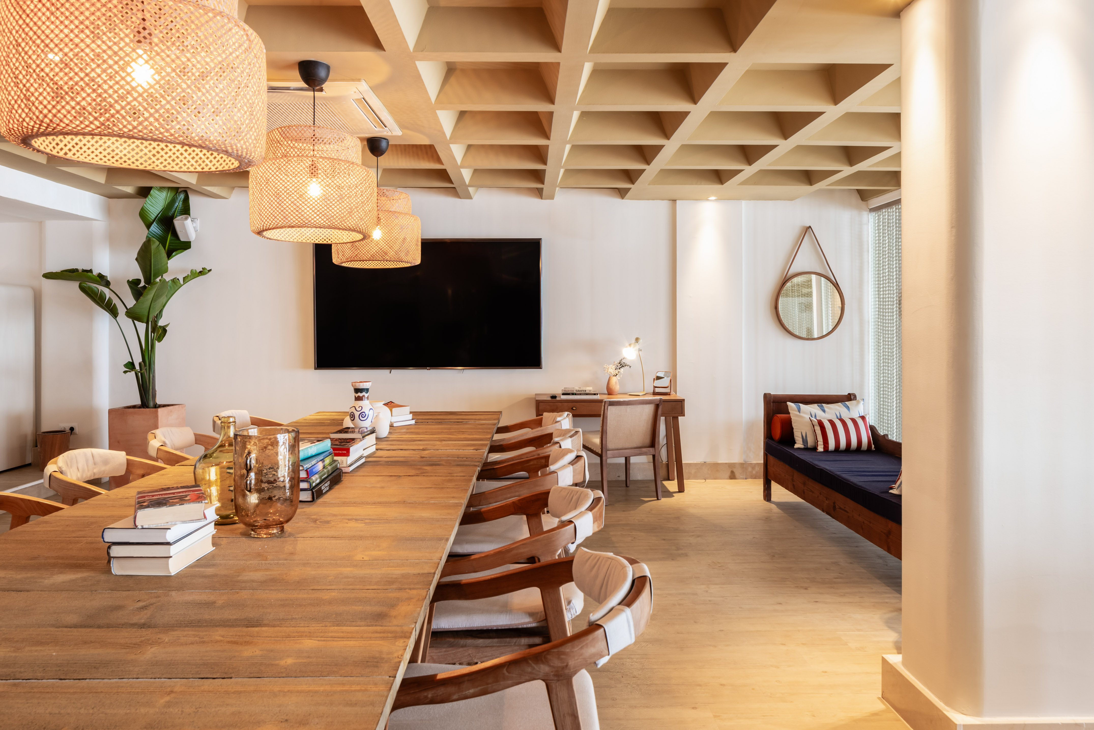 Modern communal room with long wooden table, rattan lights, and coffered ceiling.