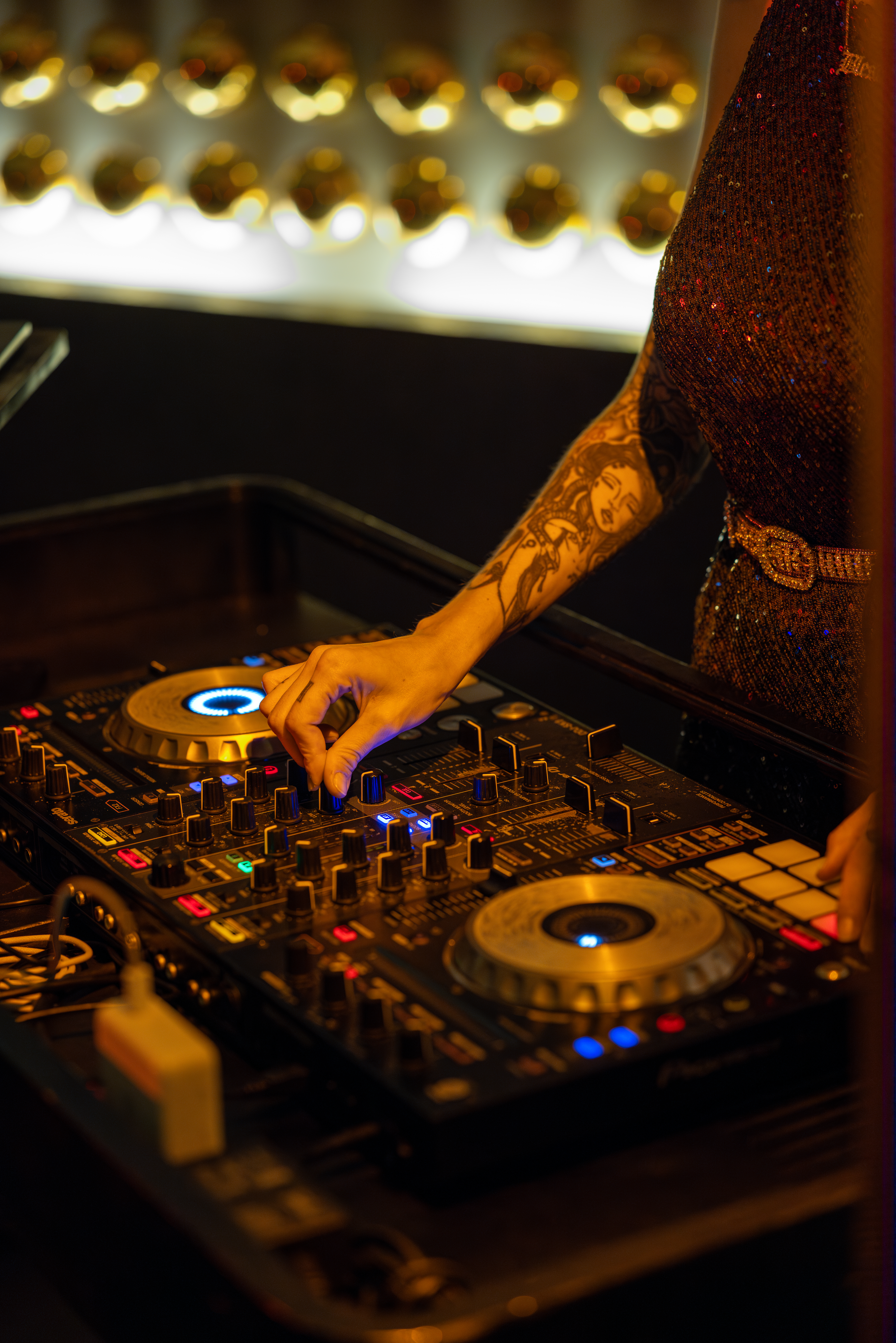 Tattooed hand mixing music on a DJ controller at a lively club.
