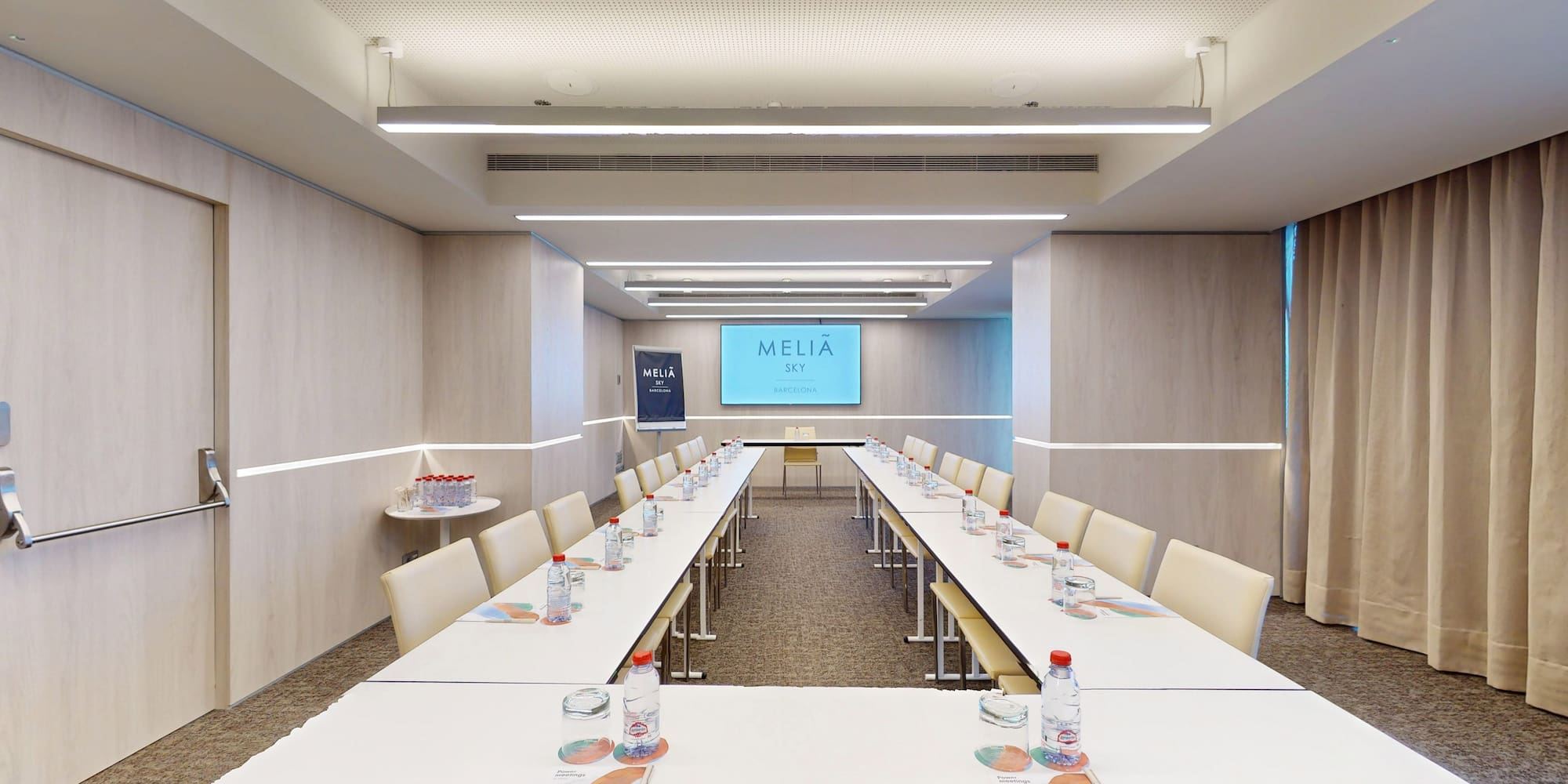 Elegant Melia Sky Barcelona meeting room with U-shaped setup and large screen.