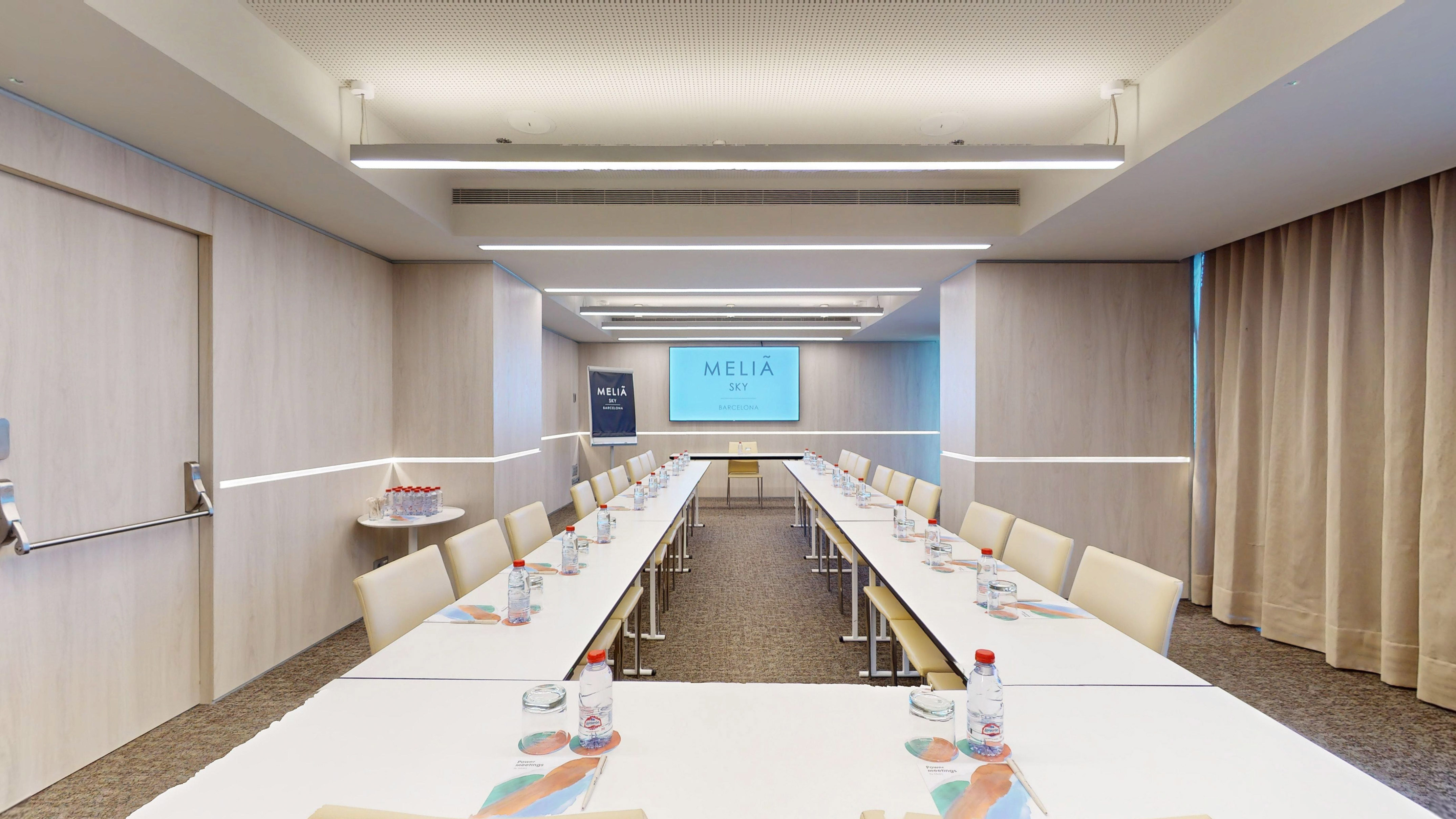 Elegant Melia Sky Barcelona meeting room with U-shaped setup and large screen.