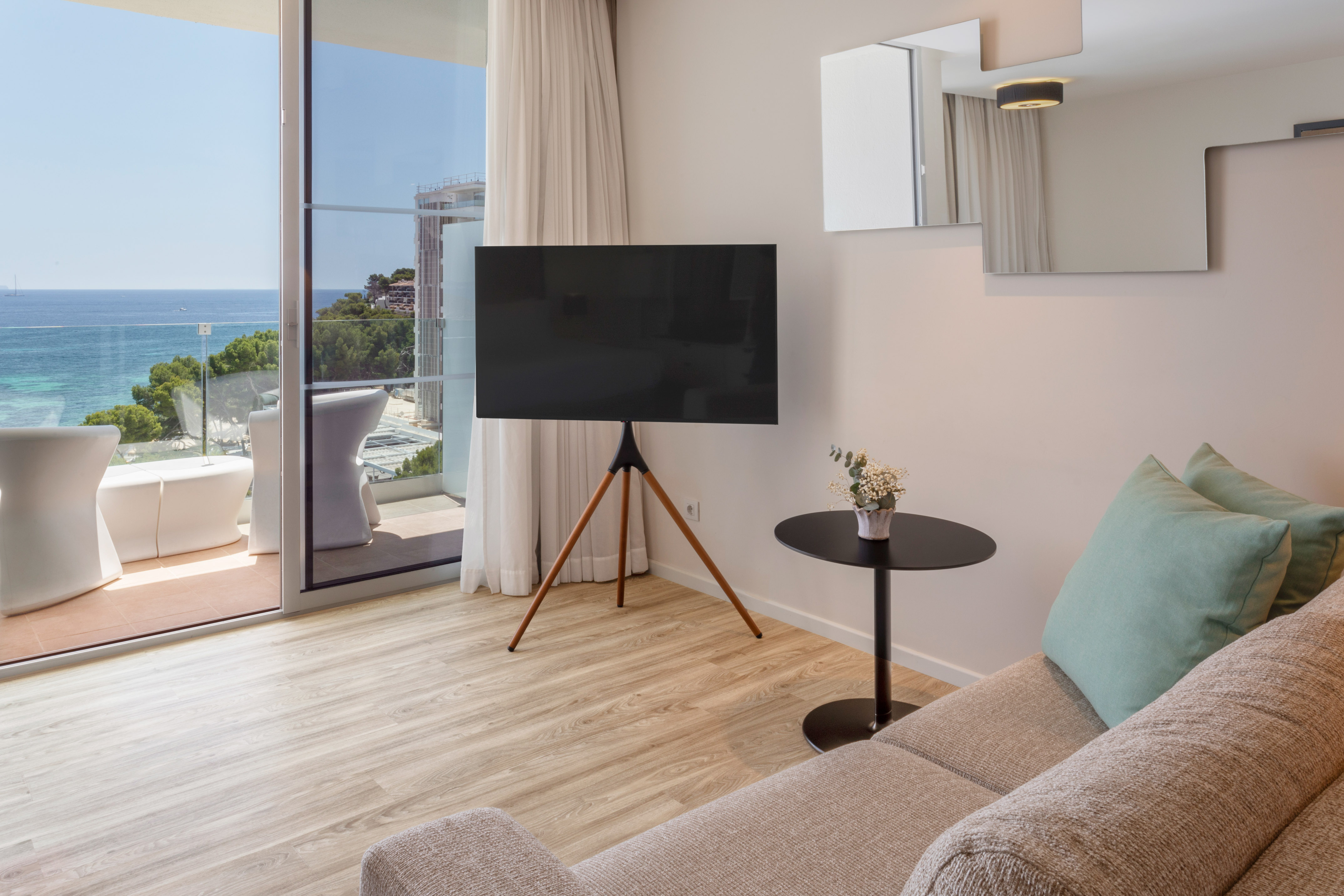 Modern hotel suite with ocean view balcony, TV, sofa, and wood floor.