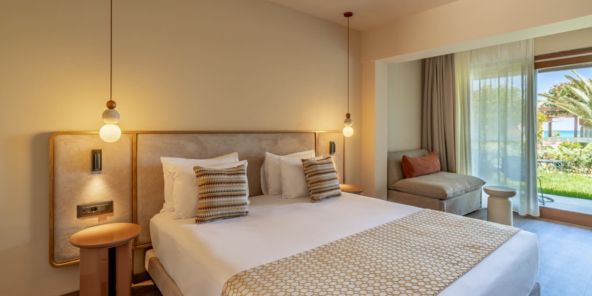 Stylish hotel bedroom with large bed, modern lighting, and balcony sea view.