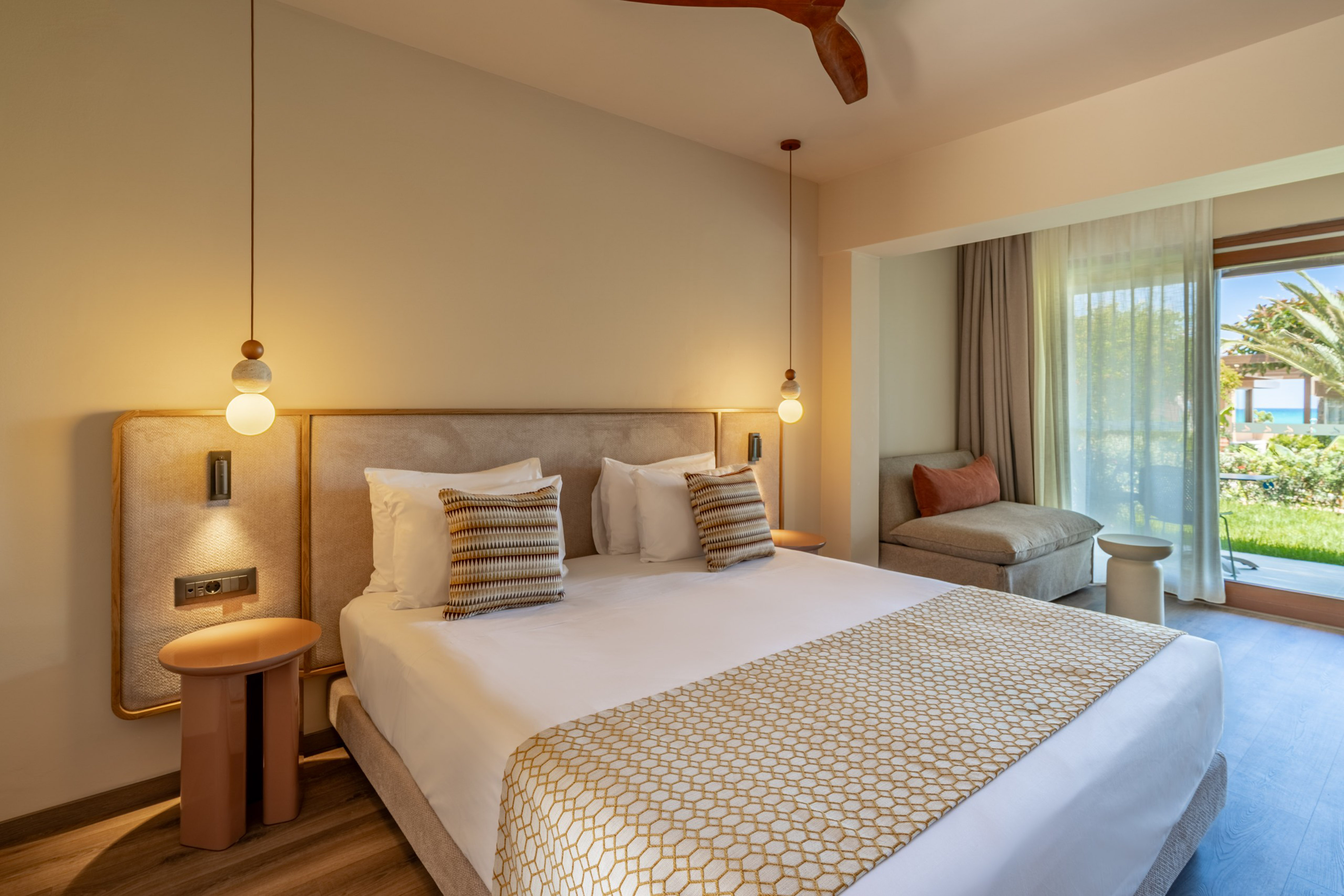 Stylish hotel bedroom with large bed, modern lighting, and balcony sea view.