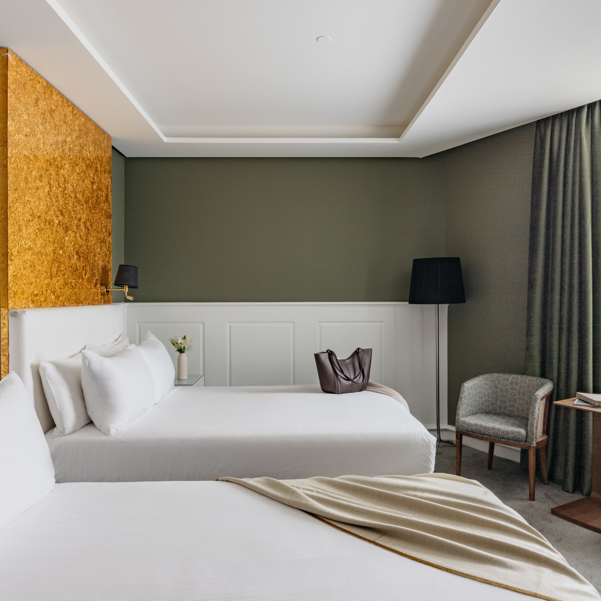 Suite hotelera con dos camas, decoración en verde oliva y detalles dorados.