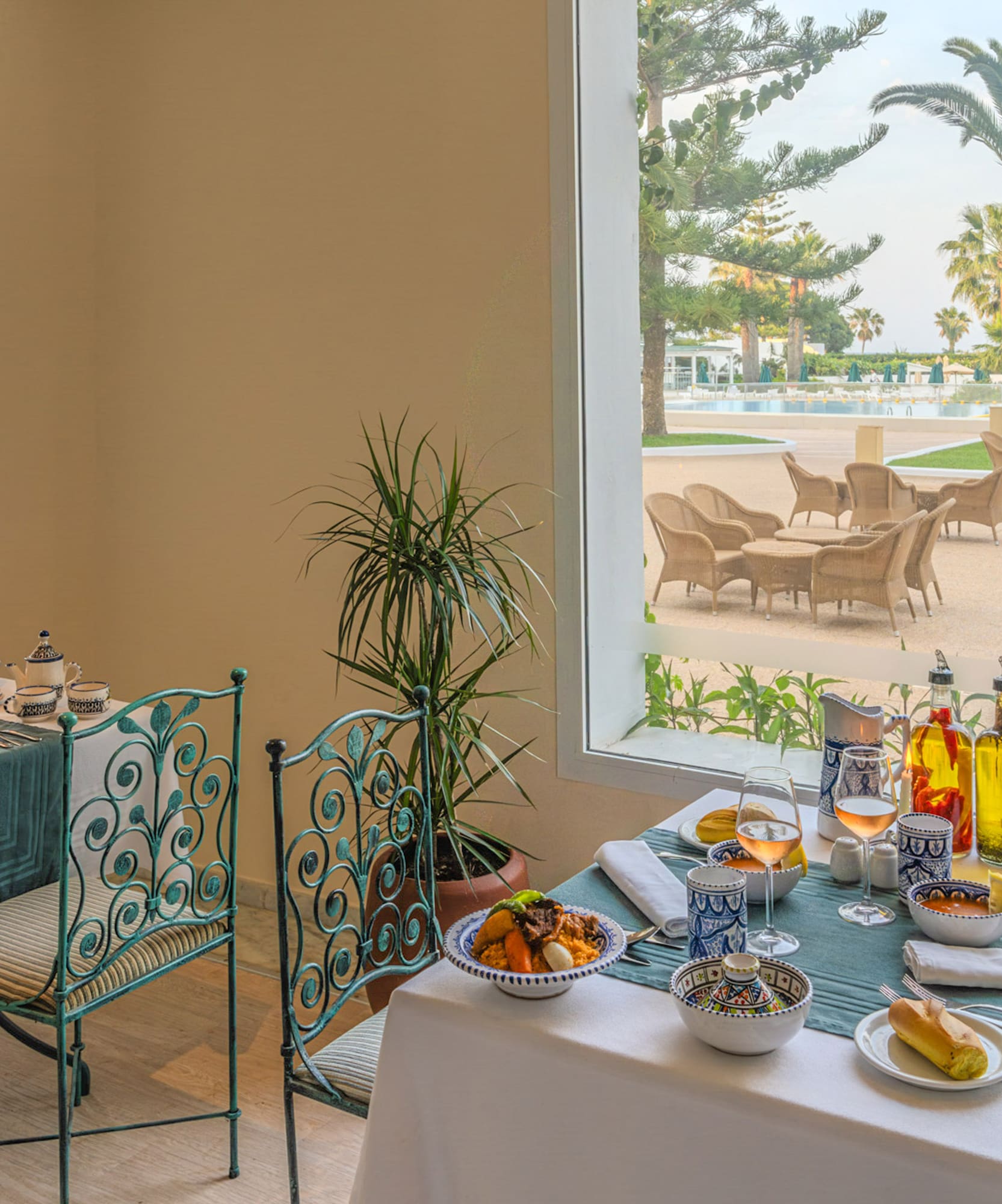 Mesa de restaurante con comida, vista a piscina, palmeras y patio de hotel.