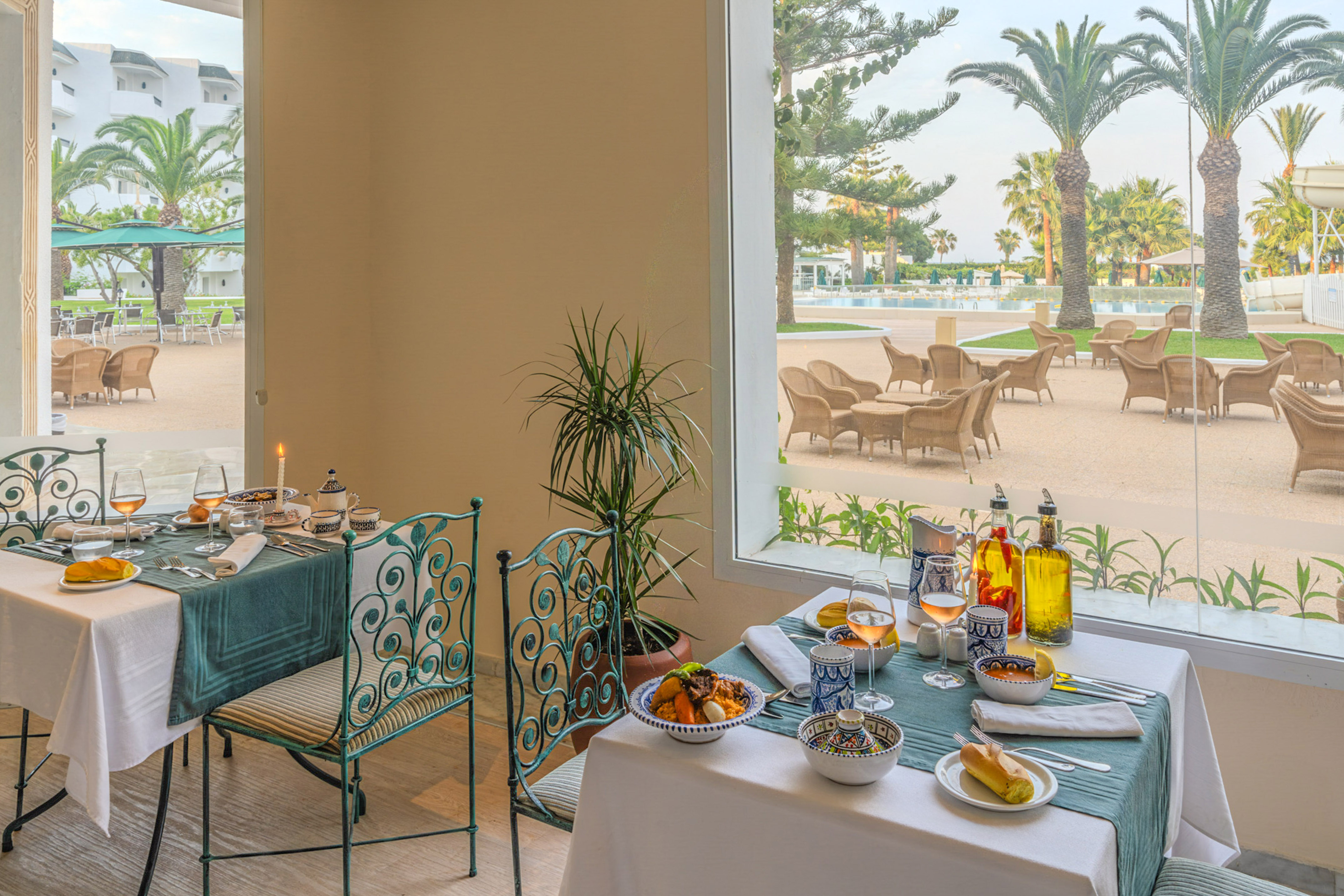 Mesa de restaurante con comida, vista a piscina, palmeras y patio de hotel.