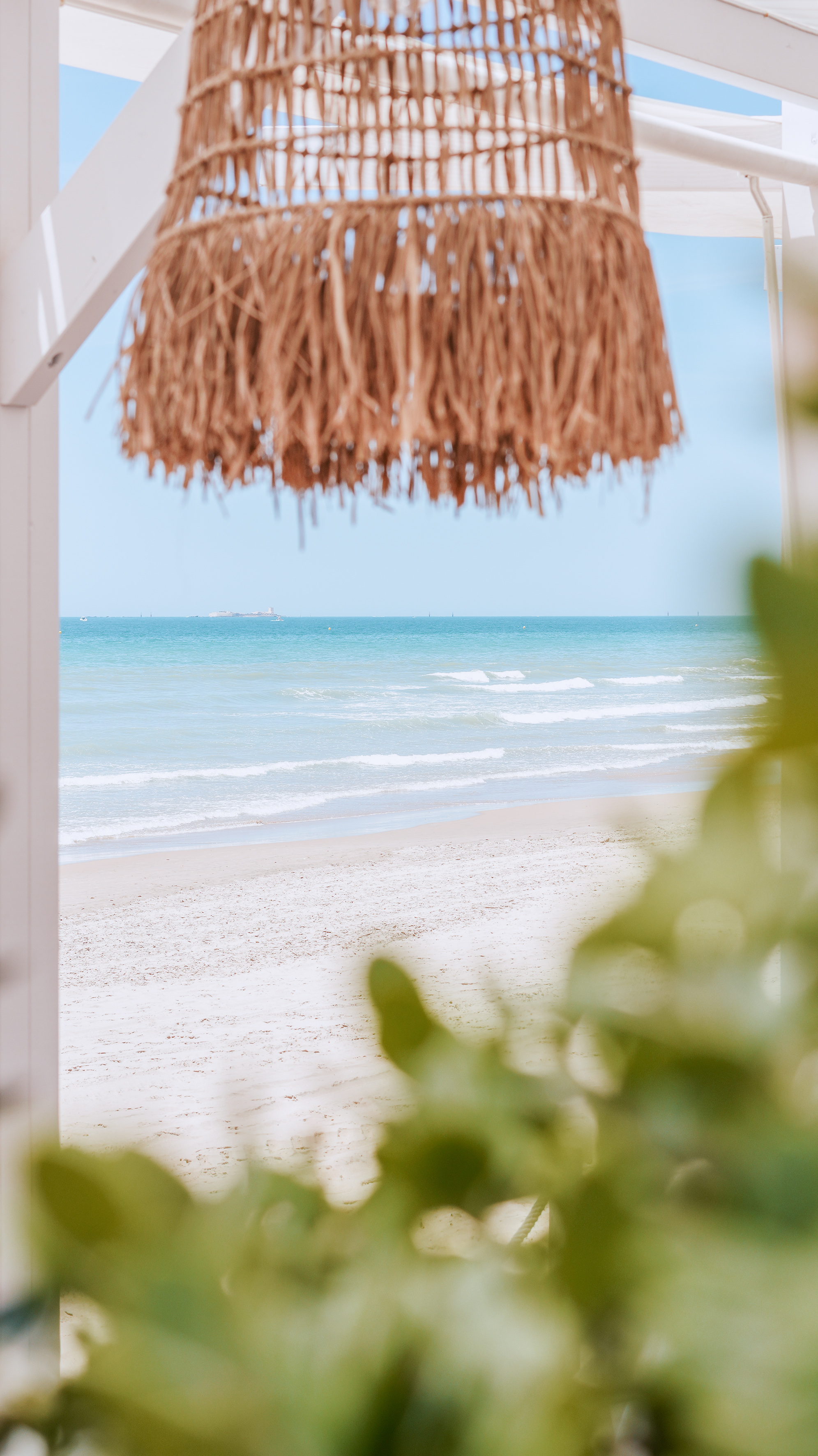 Straw pendant lamp over a calm blue ocean and sandy beach.