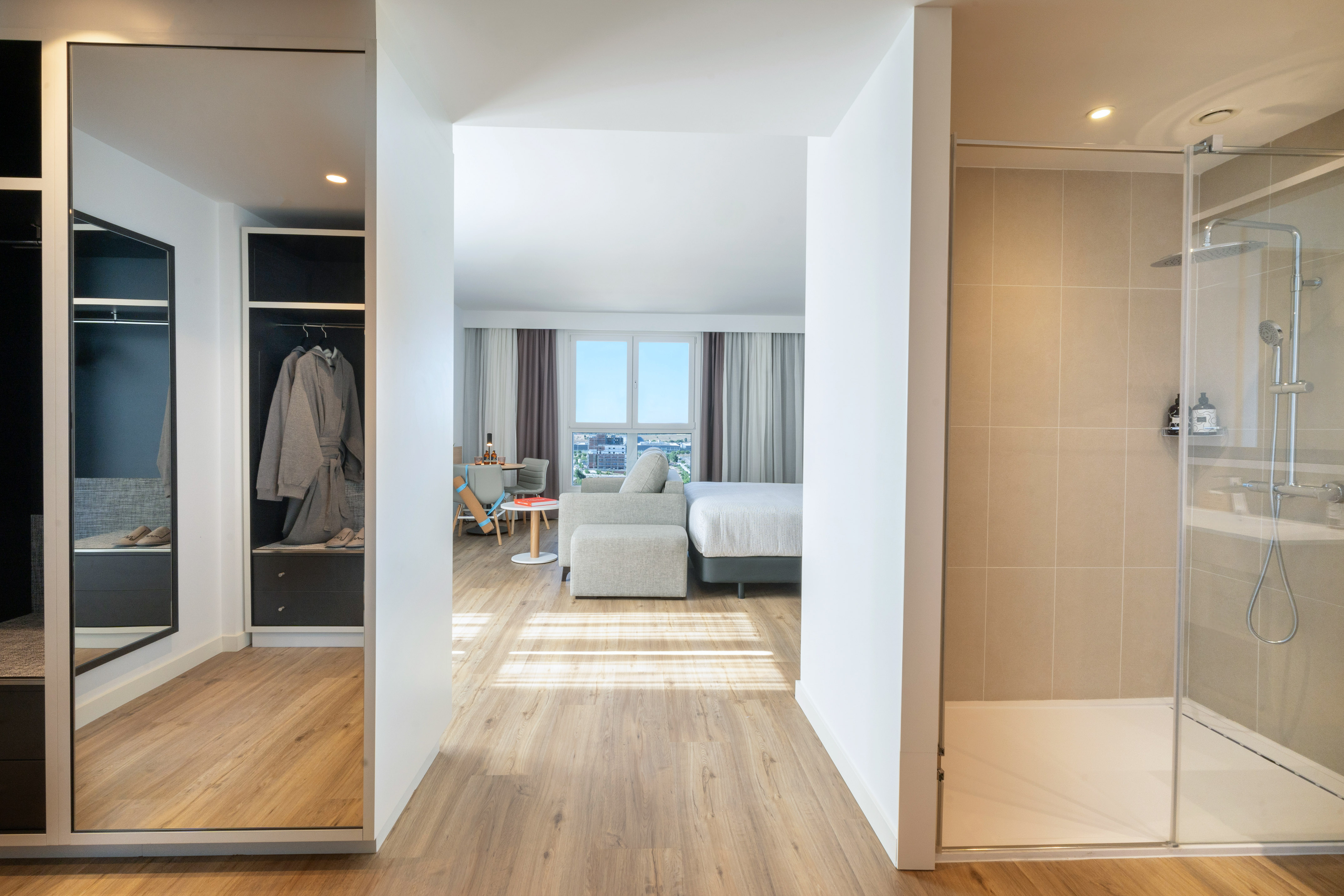 Modern hotel room with bedroom, living area, walk-in shower, and closet.