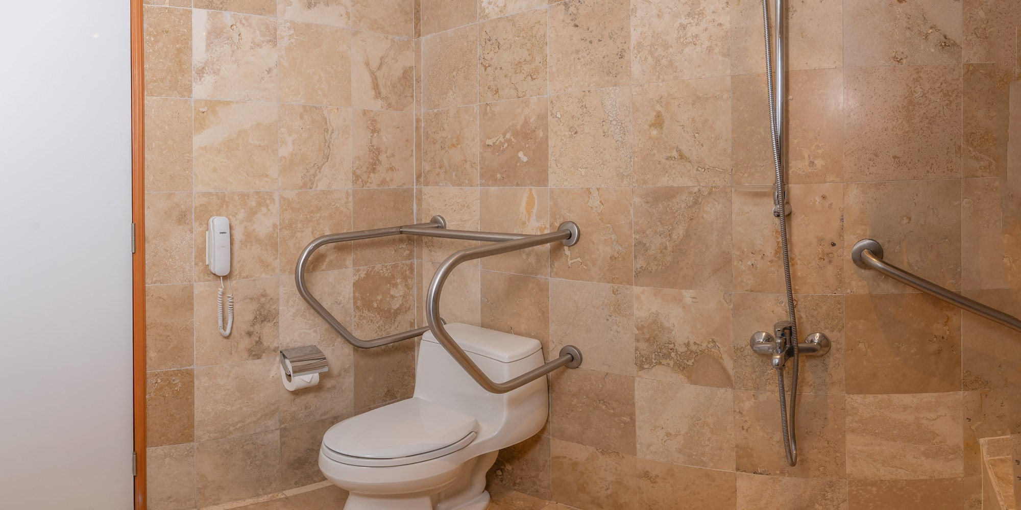 Baño accesible con inodoro, barras de apoyo, ducha y azulejos beige.