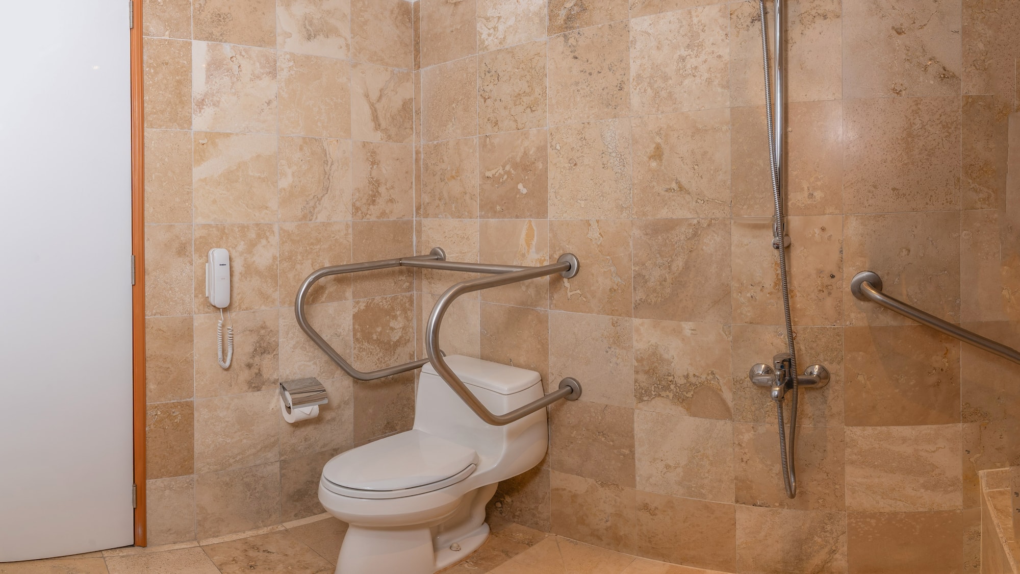 Baño accesible con inodoro, barras de apoyo, ducha y azulejos beige.
