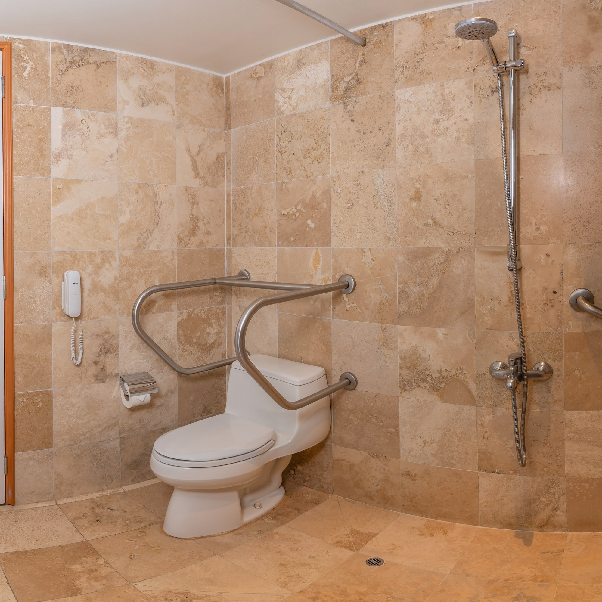 Baño accesible con inodoro, barras de apoyo, ducha y azulejos beige.