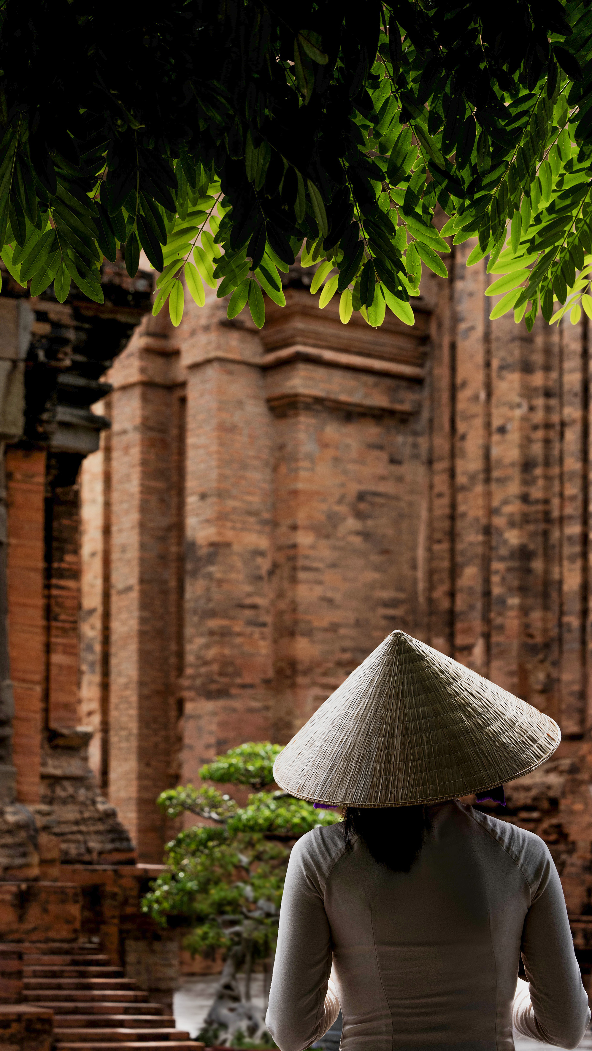 Vietnamese woman in nón lá hat at ancient brick temple.