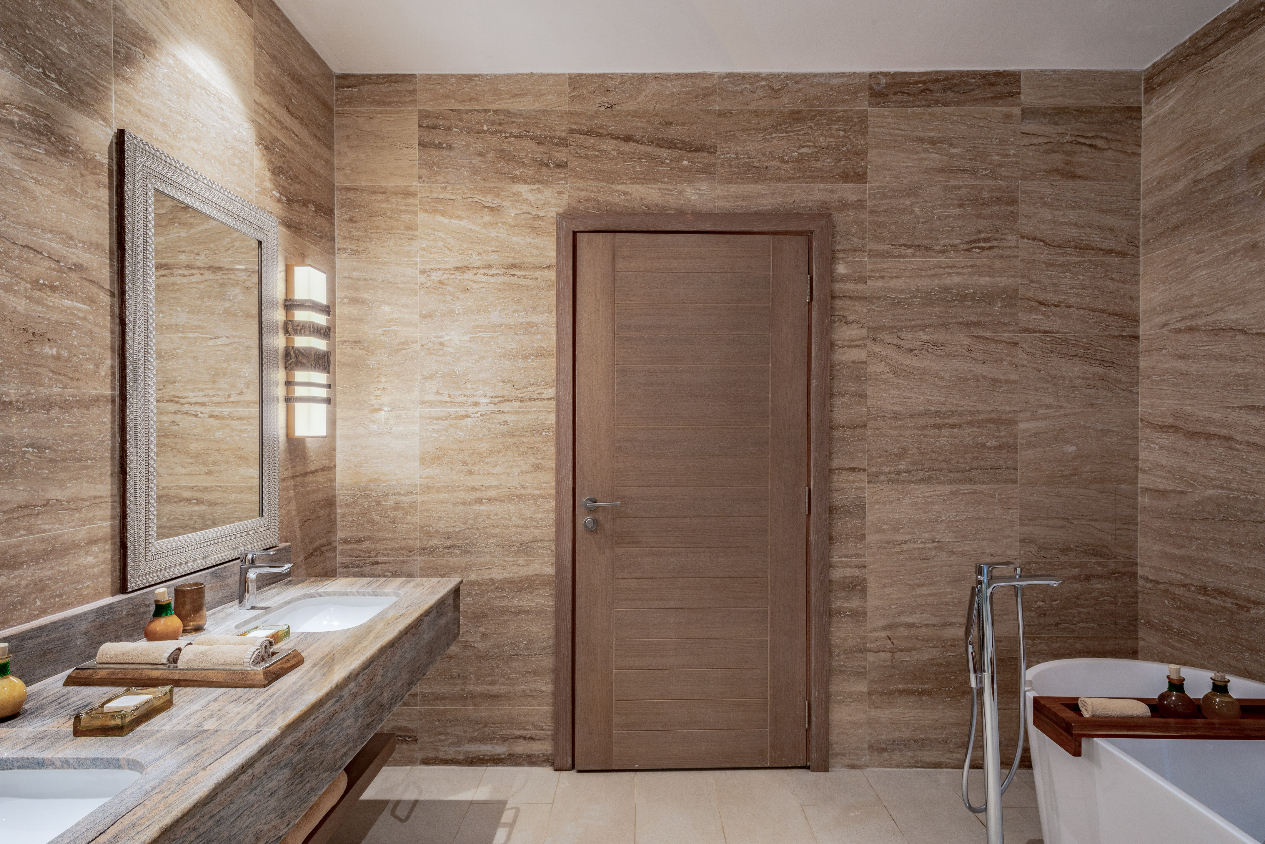 Luxury bathroom with marble walls, double vanity, ornate mirror, and freestanding tub.