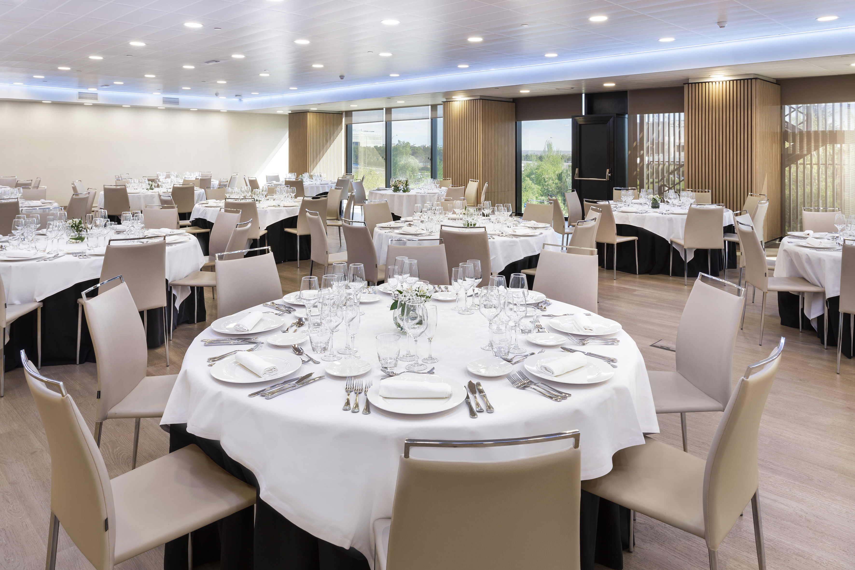 Elegant banquet hall with round tables set for formal event. Modern decor, large windows.