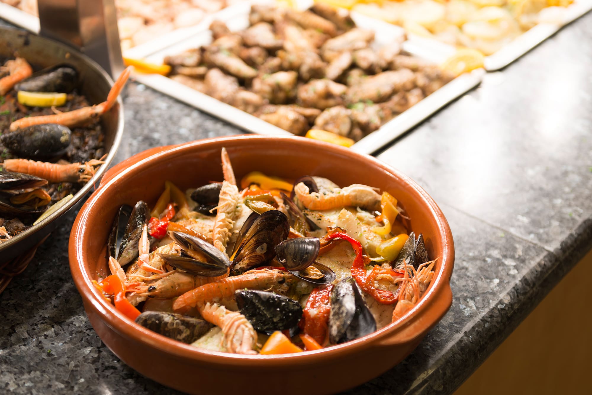 Cazuela de marisco fresco (gambas, mejillones) y paella negra en buffet.