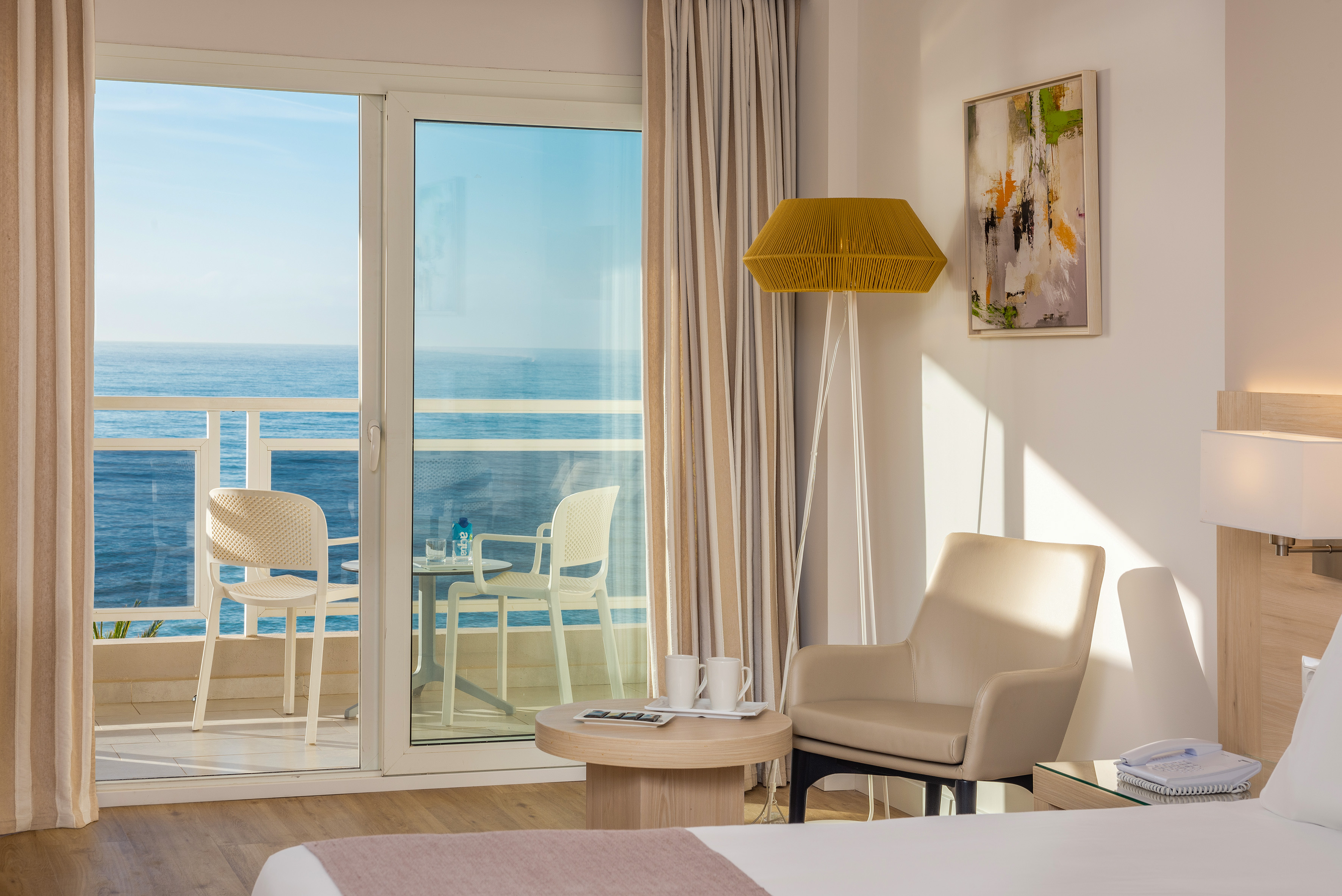 Hotel room with ocean view balcony, white outdoor furniture, and modern interior.