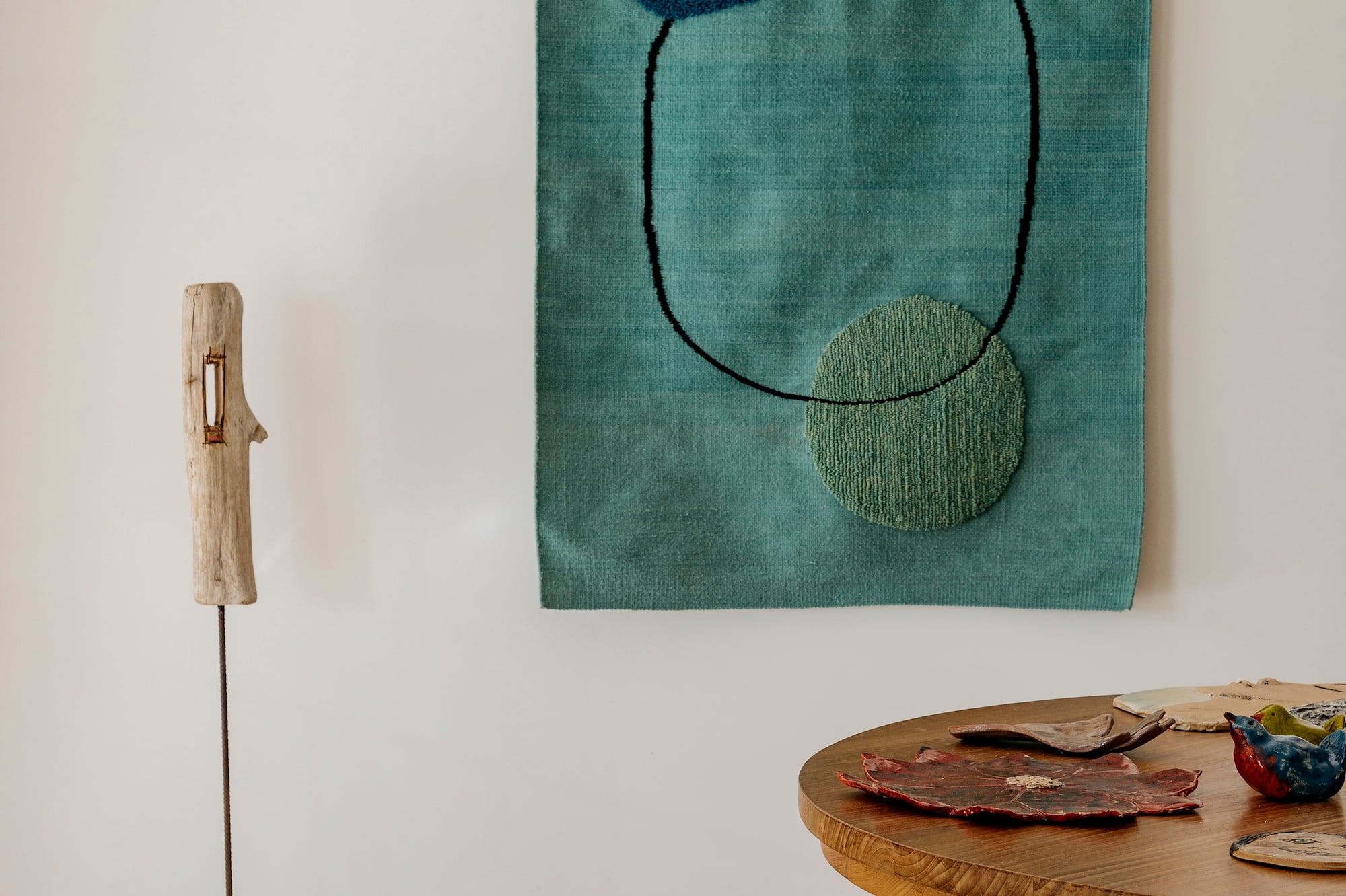 Teal abstract wall art, wooden sculpture, round table, vintage rug.