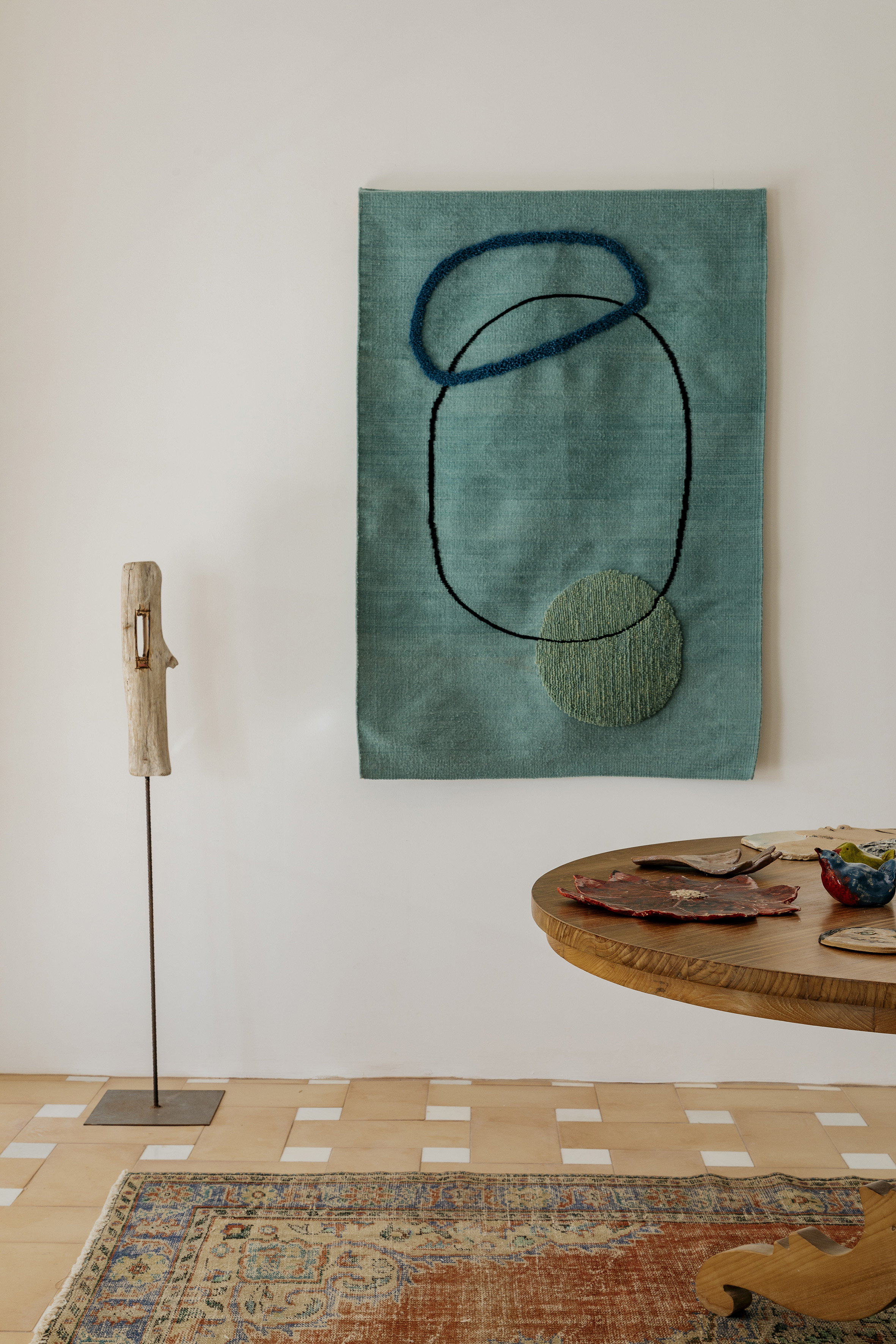 Teal abstract wall art, wooden sculpture, round table, vintage rug.