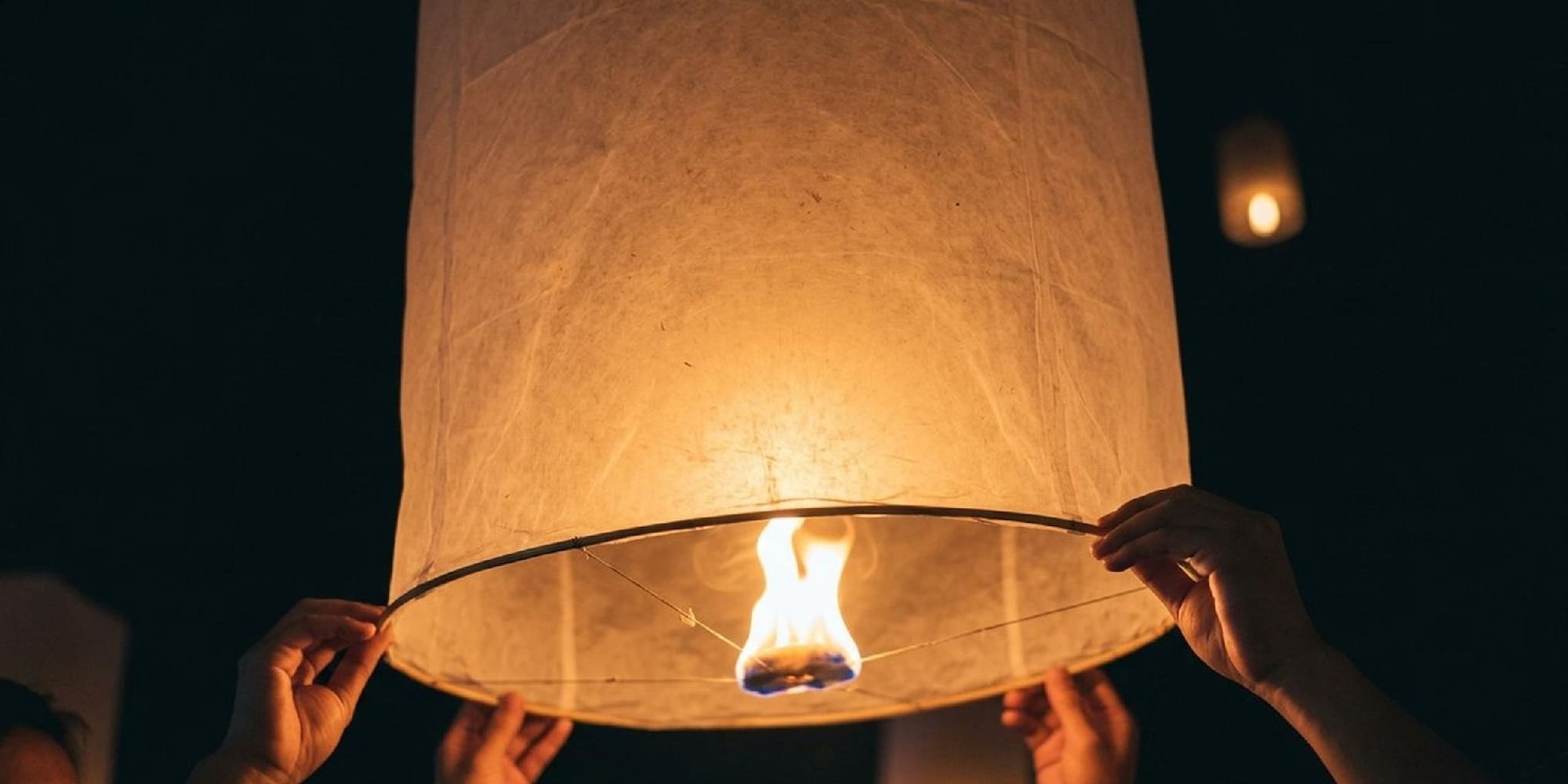 Lit sky lantern held by hands, flame visible, night festival.