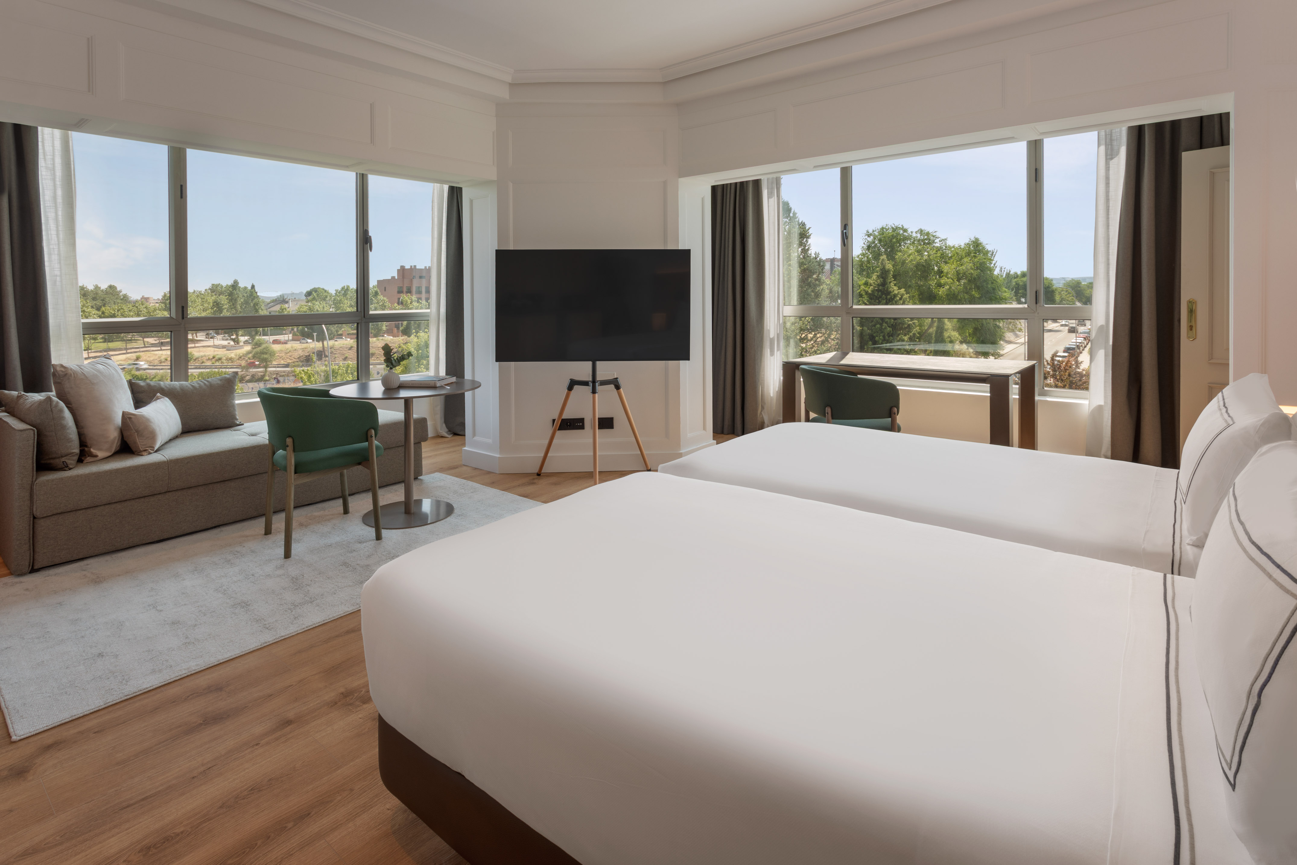 Hotel room with twin beds, panoramic city view, sofa, and modern amenities.