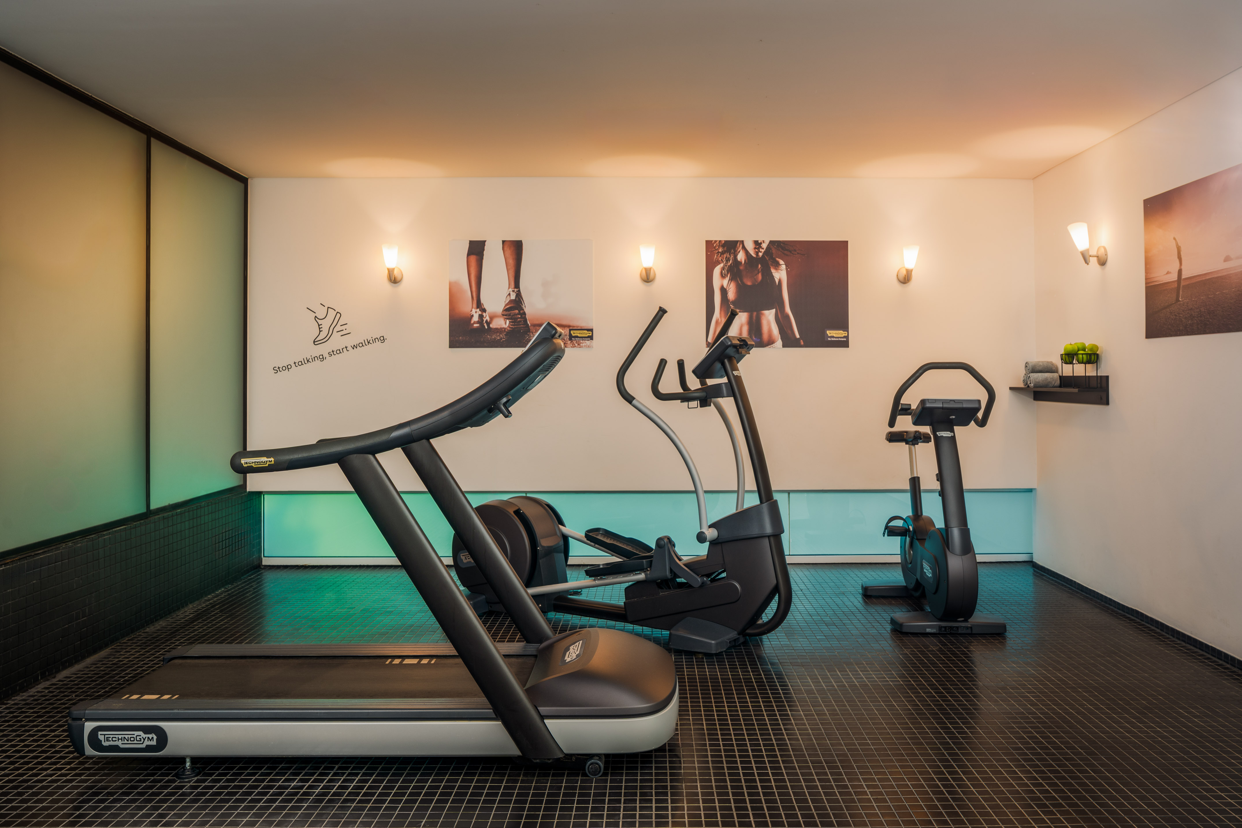 Modern gym with Technogym treadmill, elliptical, and stationary bike.
