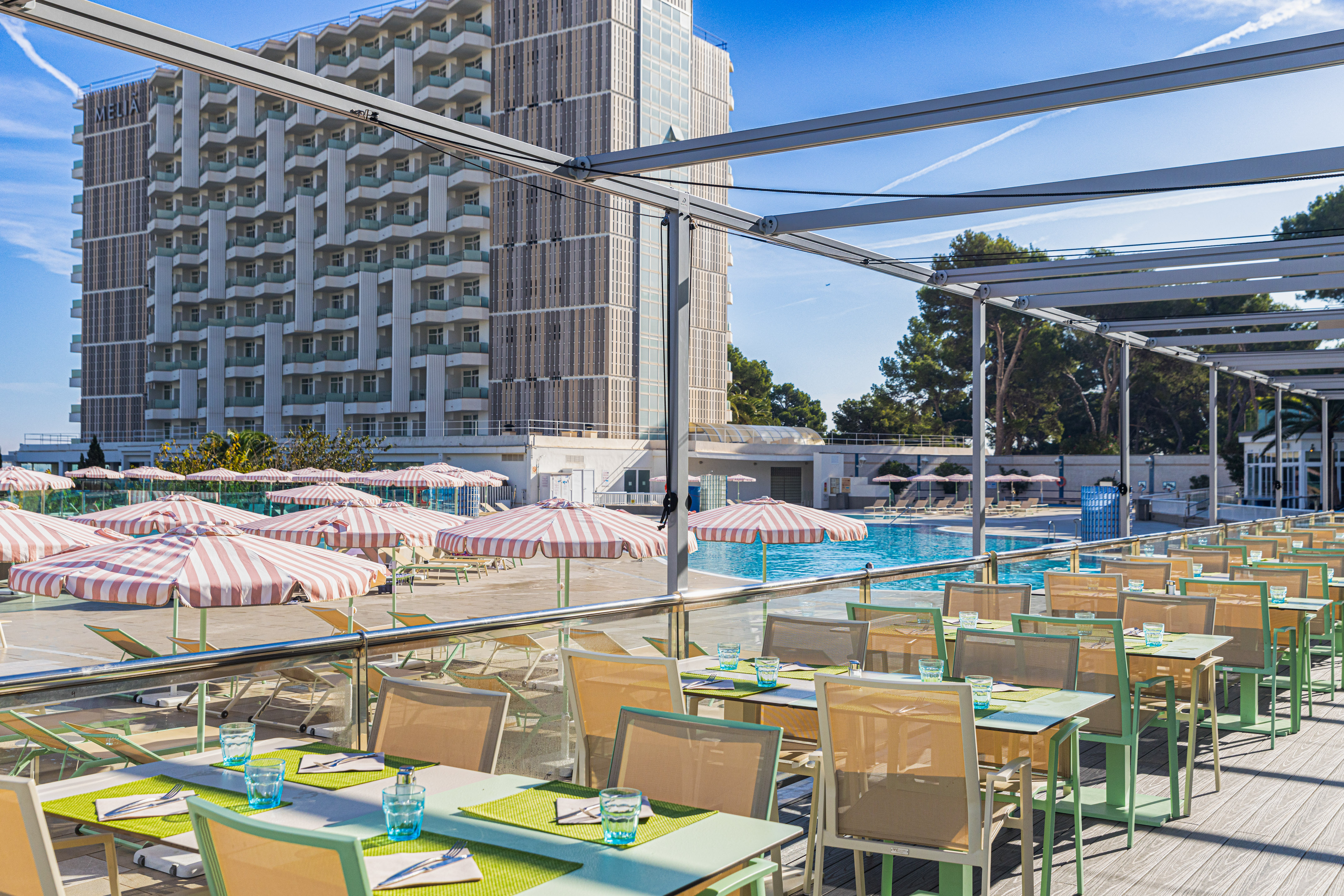 Outdoor dining terrace at Meliá hotel resort, overlooking pool with lounge chairs.