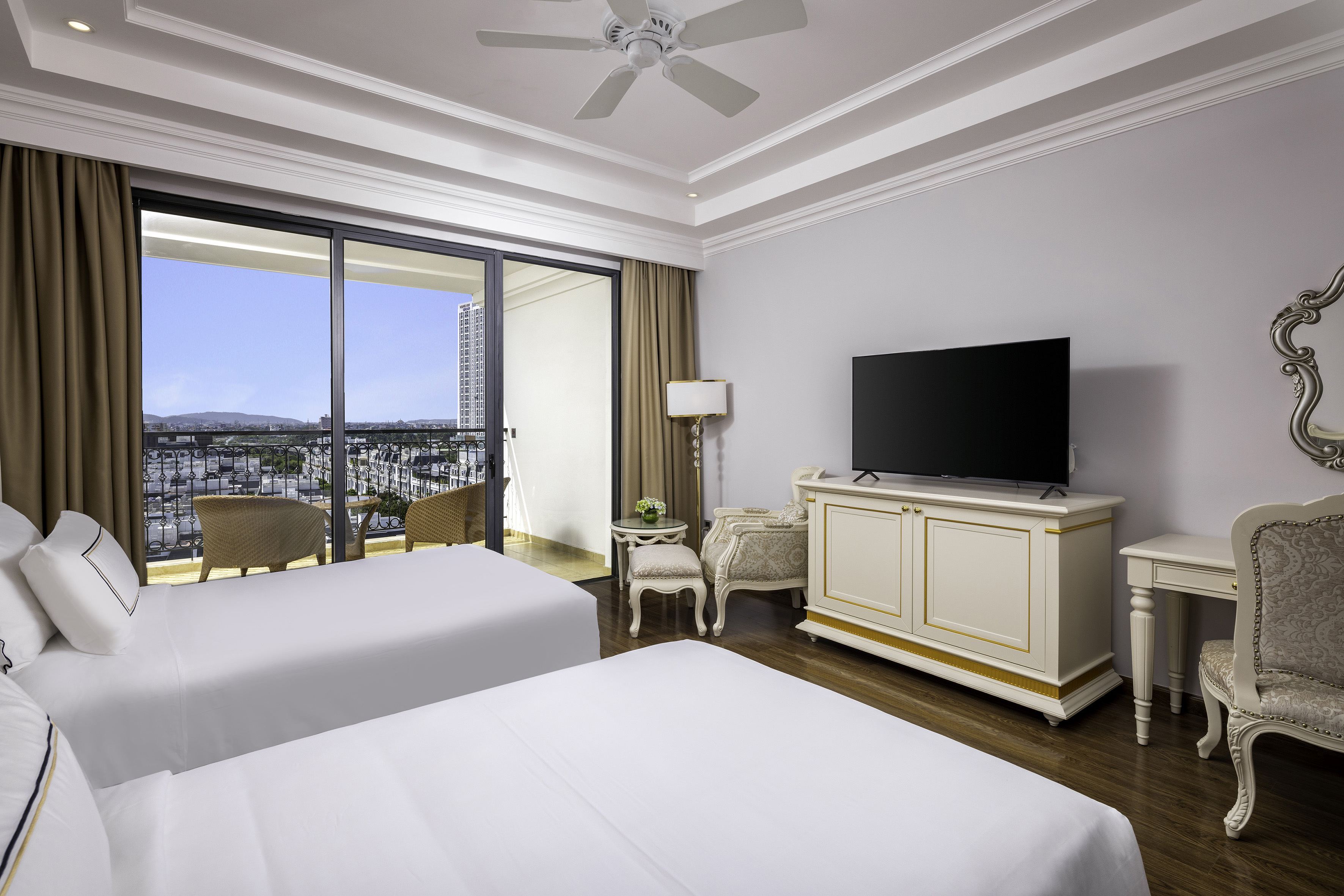 Elegant hotel twin room with balcony city view, TV, and classic furnishings.