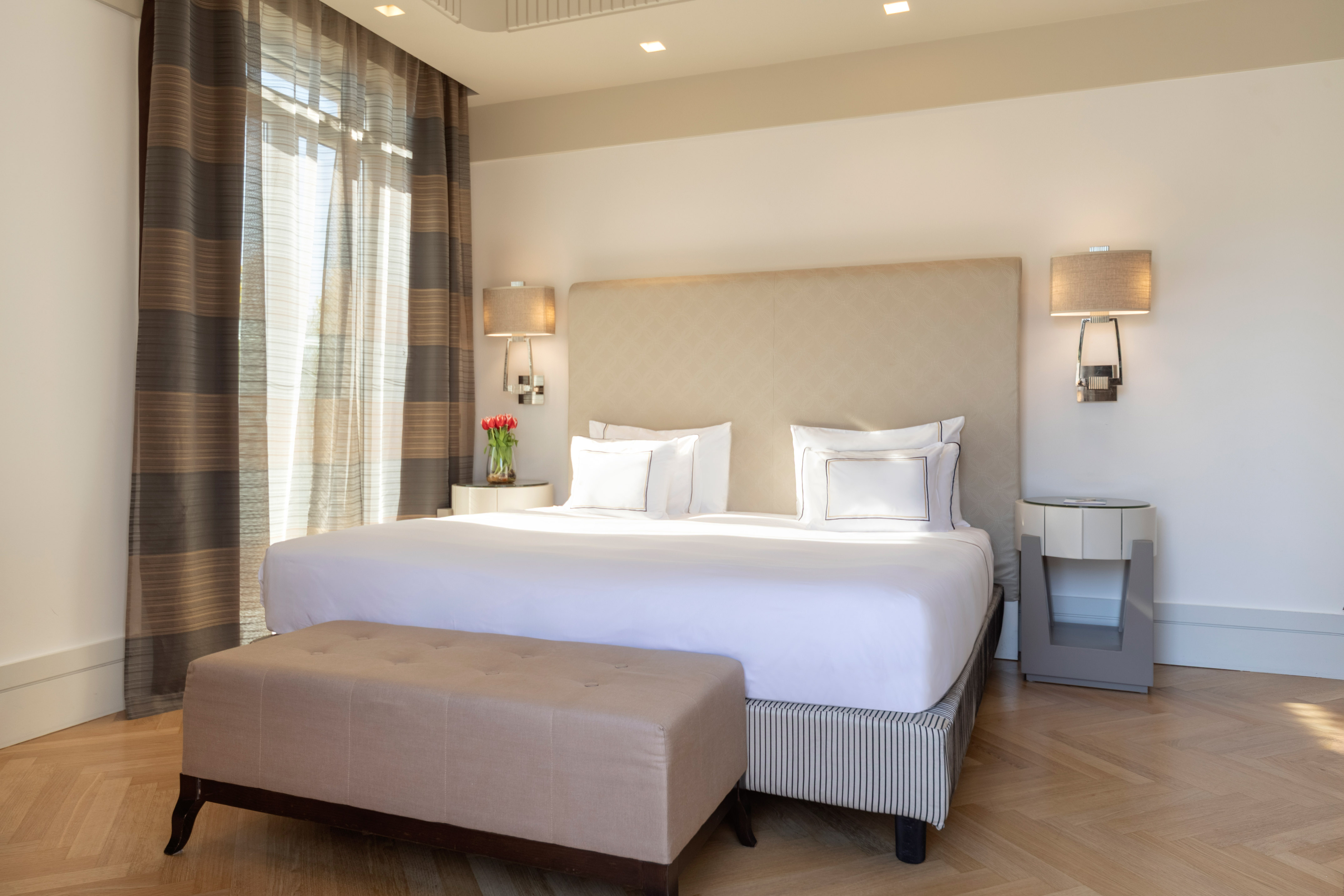Modern hotel bedroom with king bed, elegant decor, natural light, and wood floor.