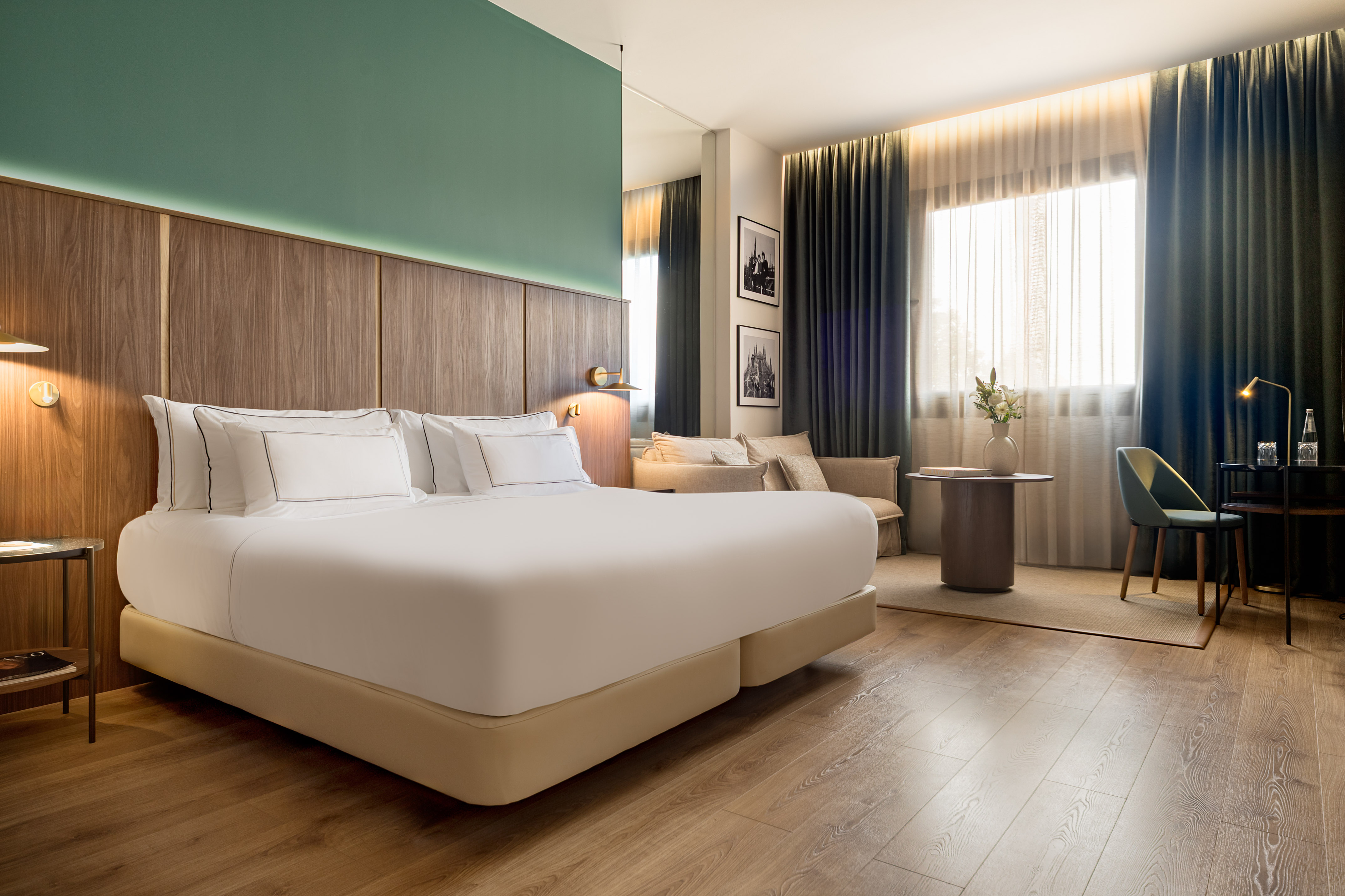 Modern hotel bedroom with king bed, wooden headboard, and green accent wall.