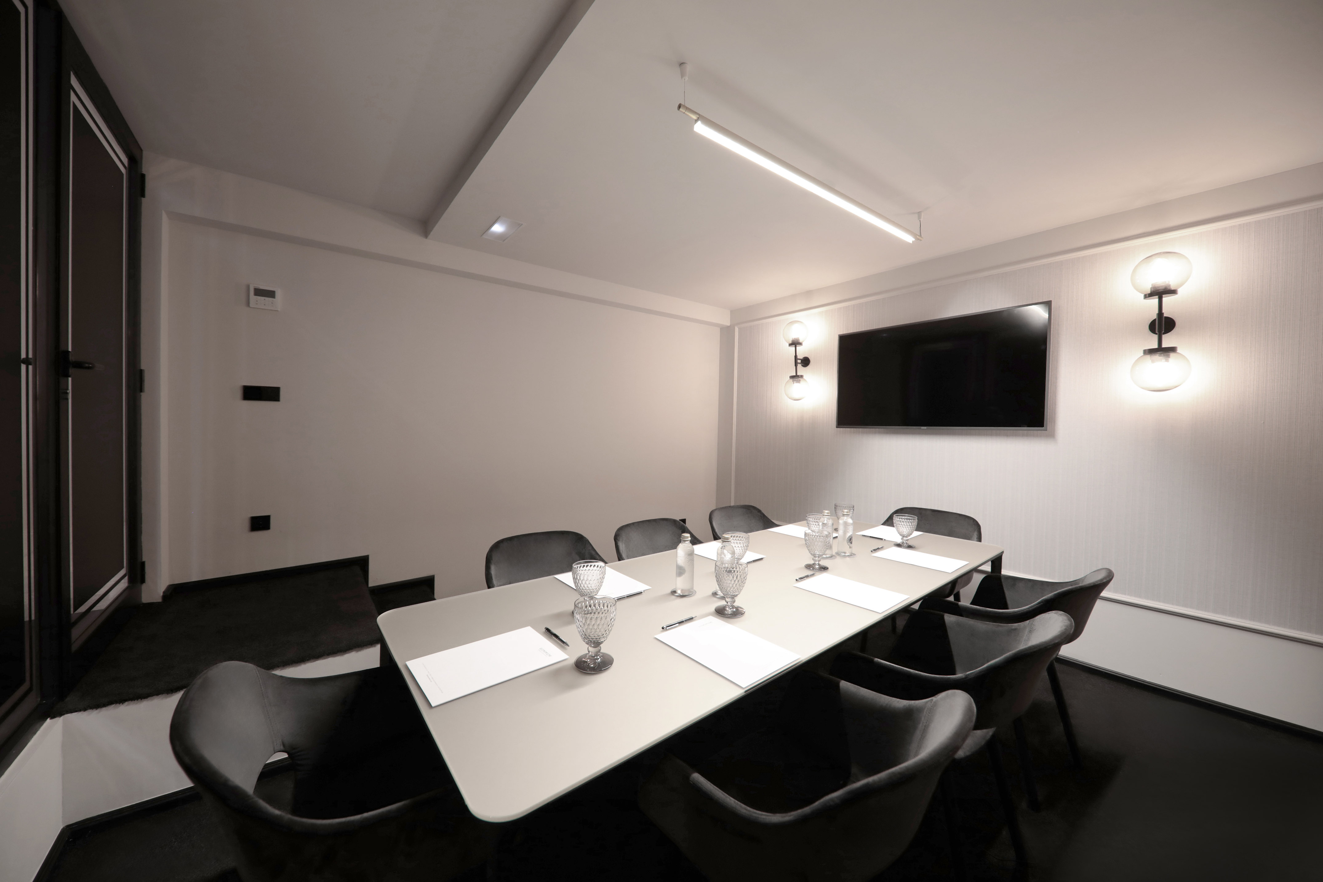 Modern conference room with grey table, chairs, wall TV, and sleek lighting.