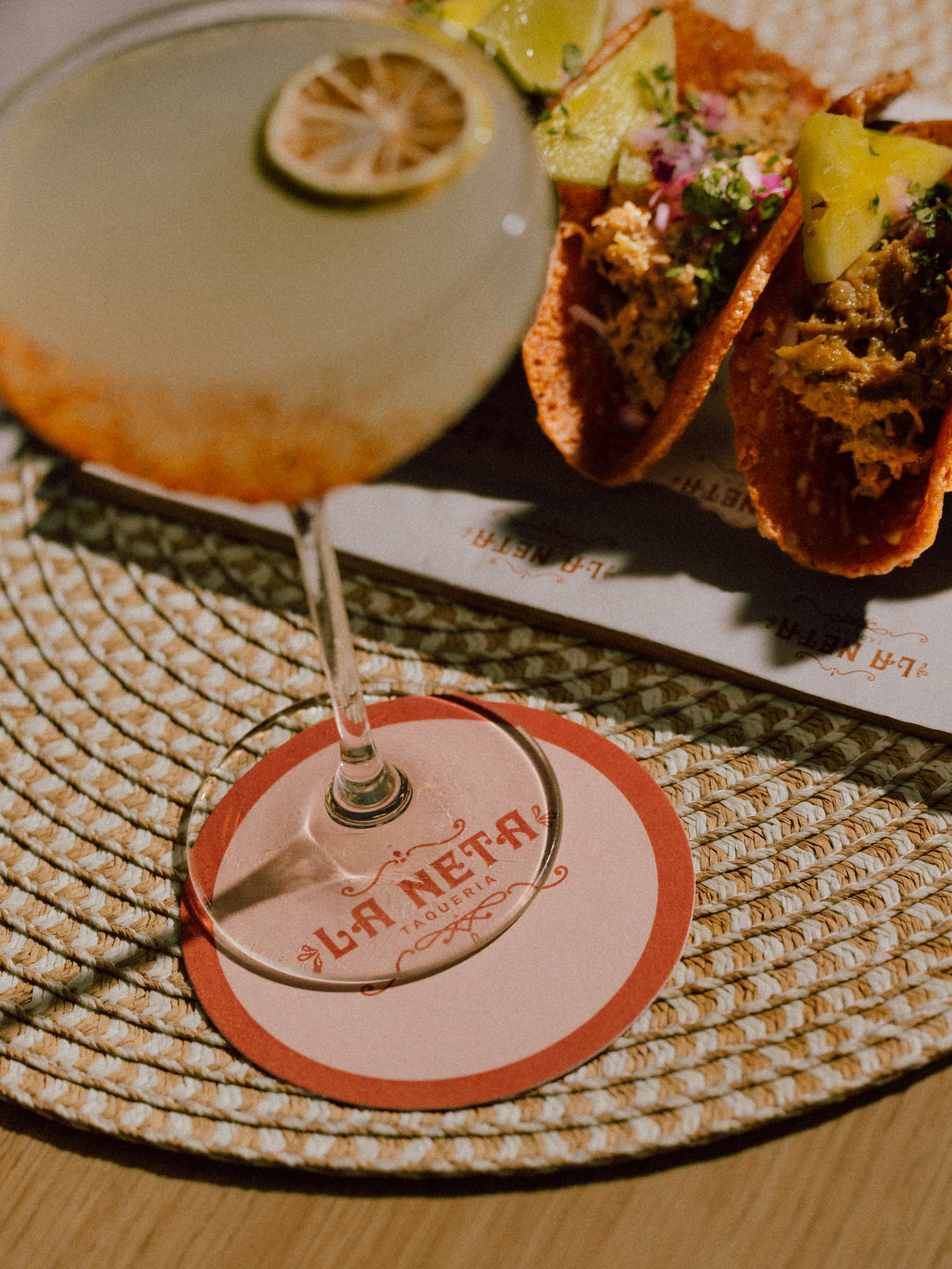 Cocktail with lime, street tacos, and La Neta Taqueria coaster.