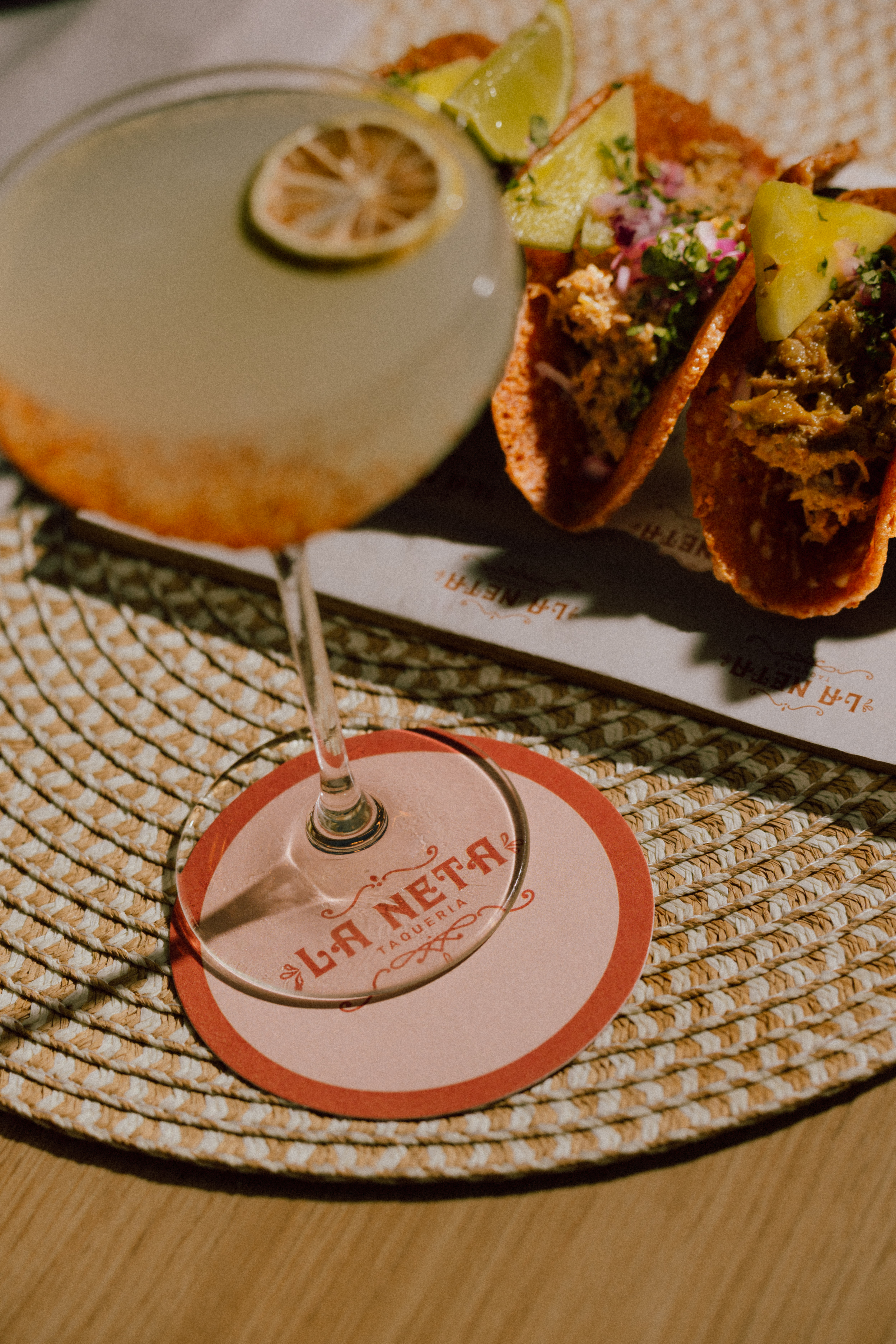 Cocktail with lime, street tacos, and La Neta Taqueria coaster.
