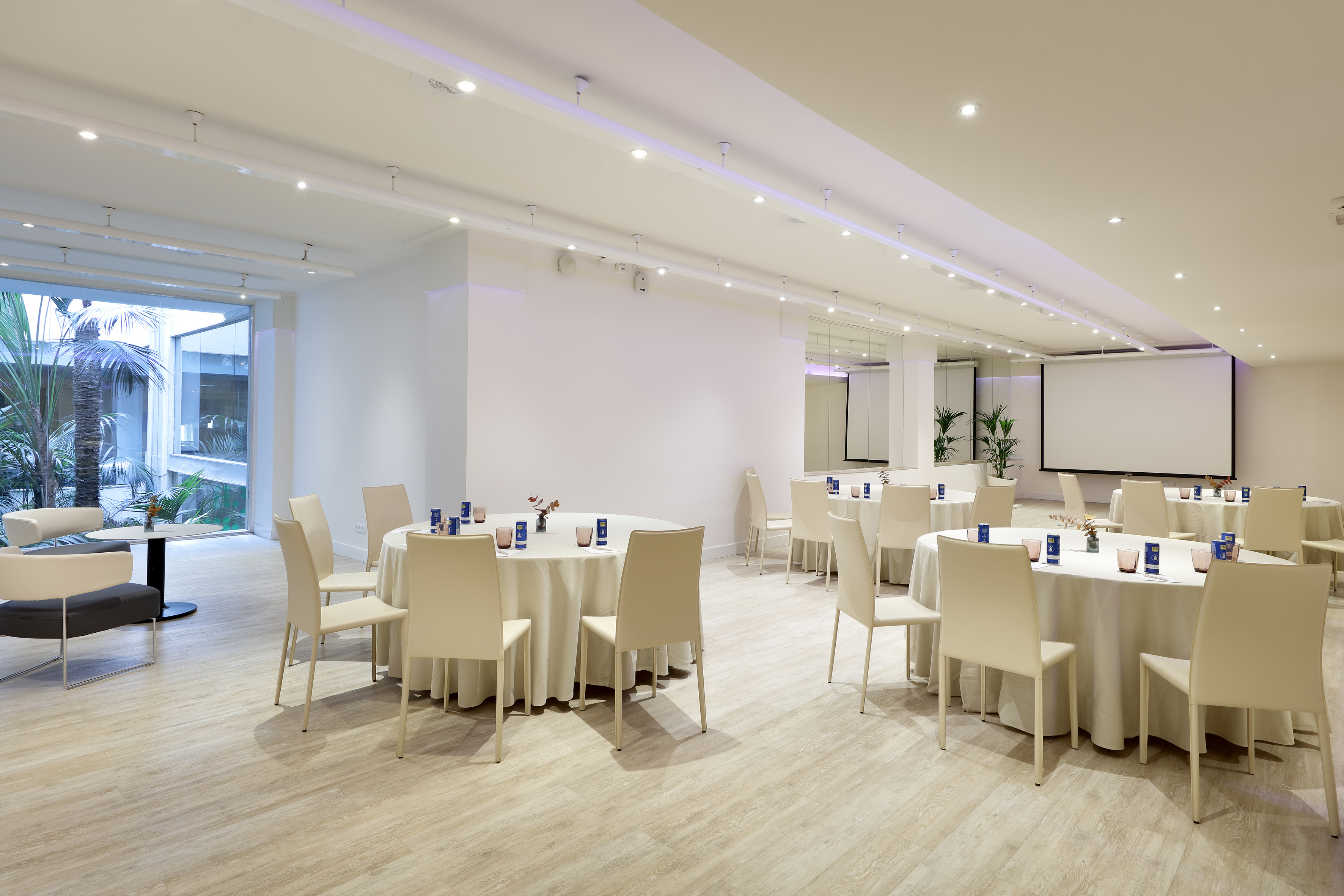 Modern meeting room with round tables, projector screen, and natural light.