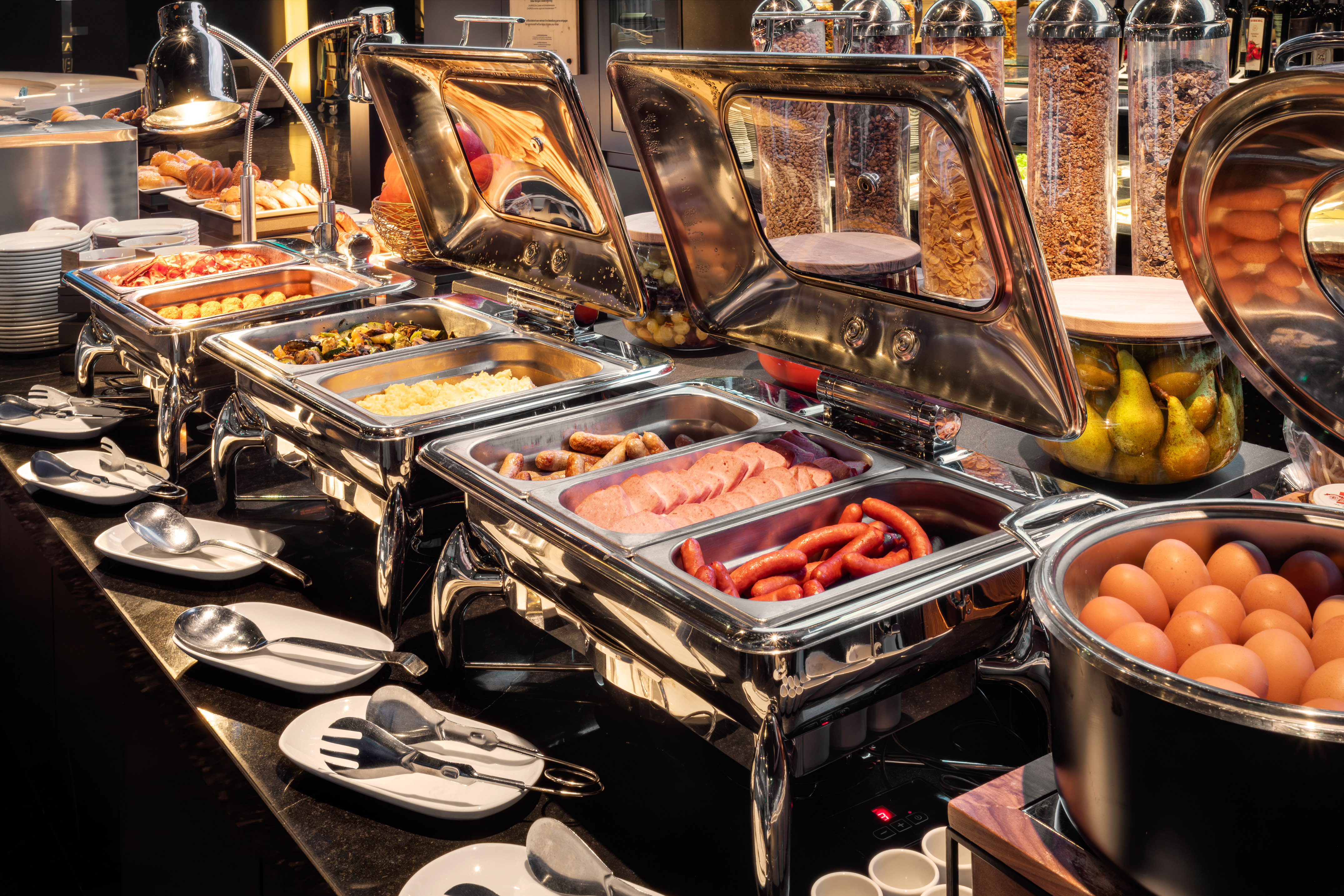 Hotel breakfast buffet: hot eggs, sausages, bacon, pastries, and cereals.