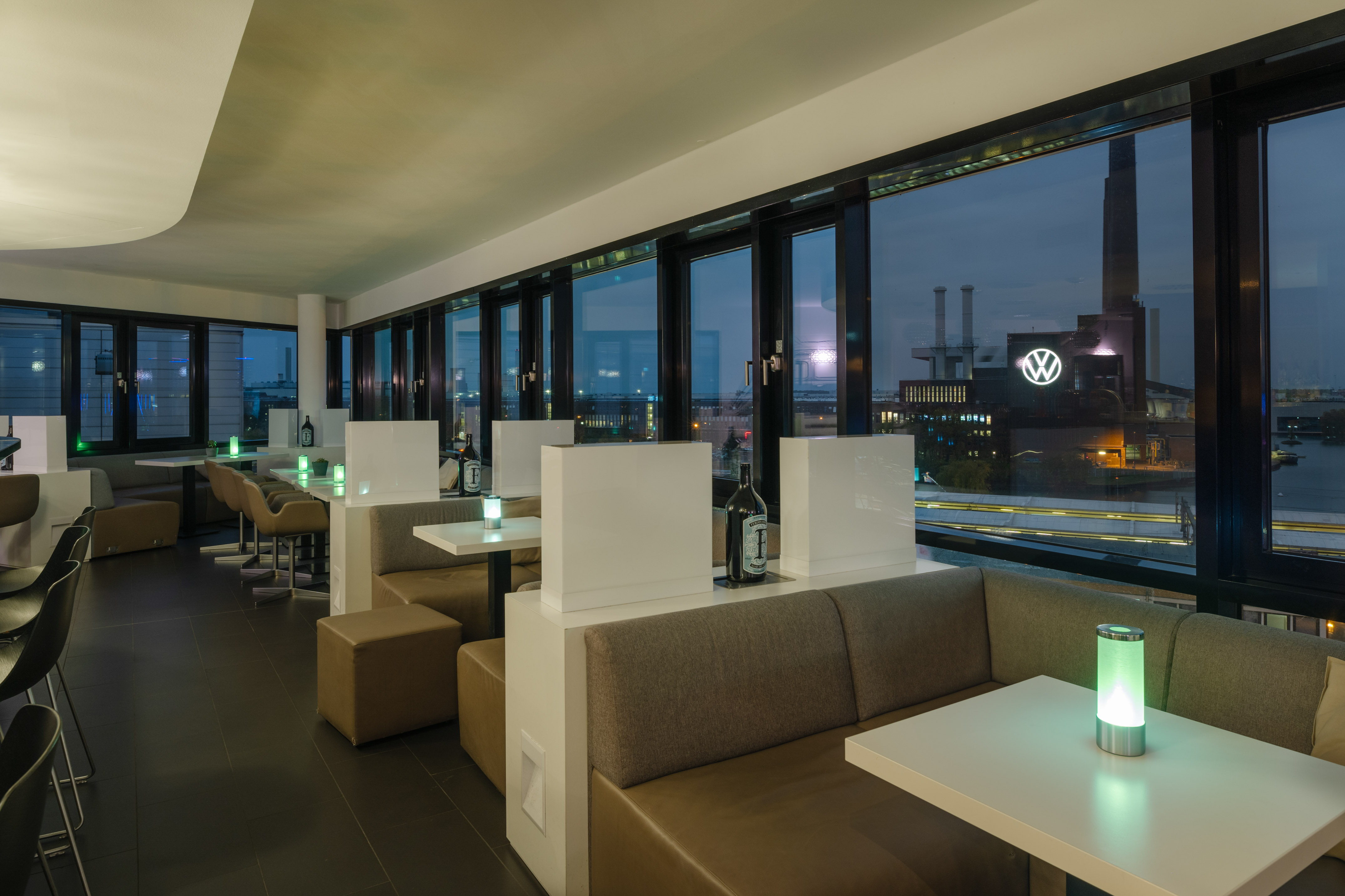 Modern bar with evening city view, illuminated VW logo, booth seating.