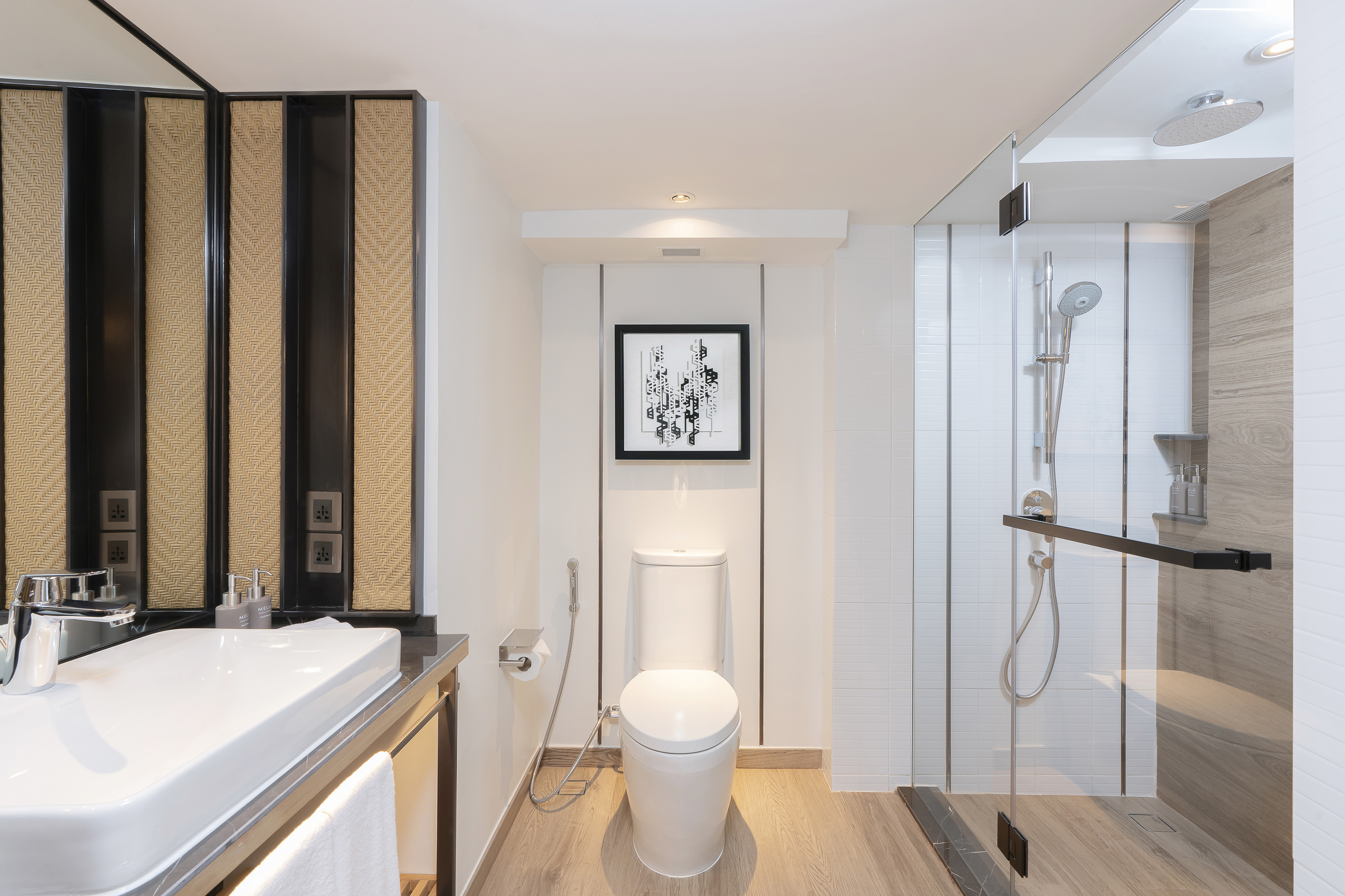 Clean modern bathroom with white sink, toilet, glass shower, and light wood floor.