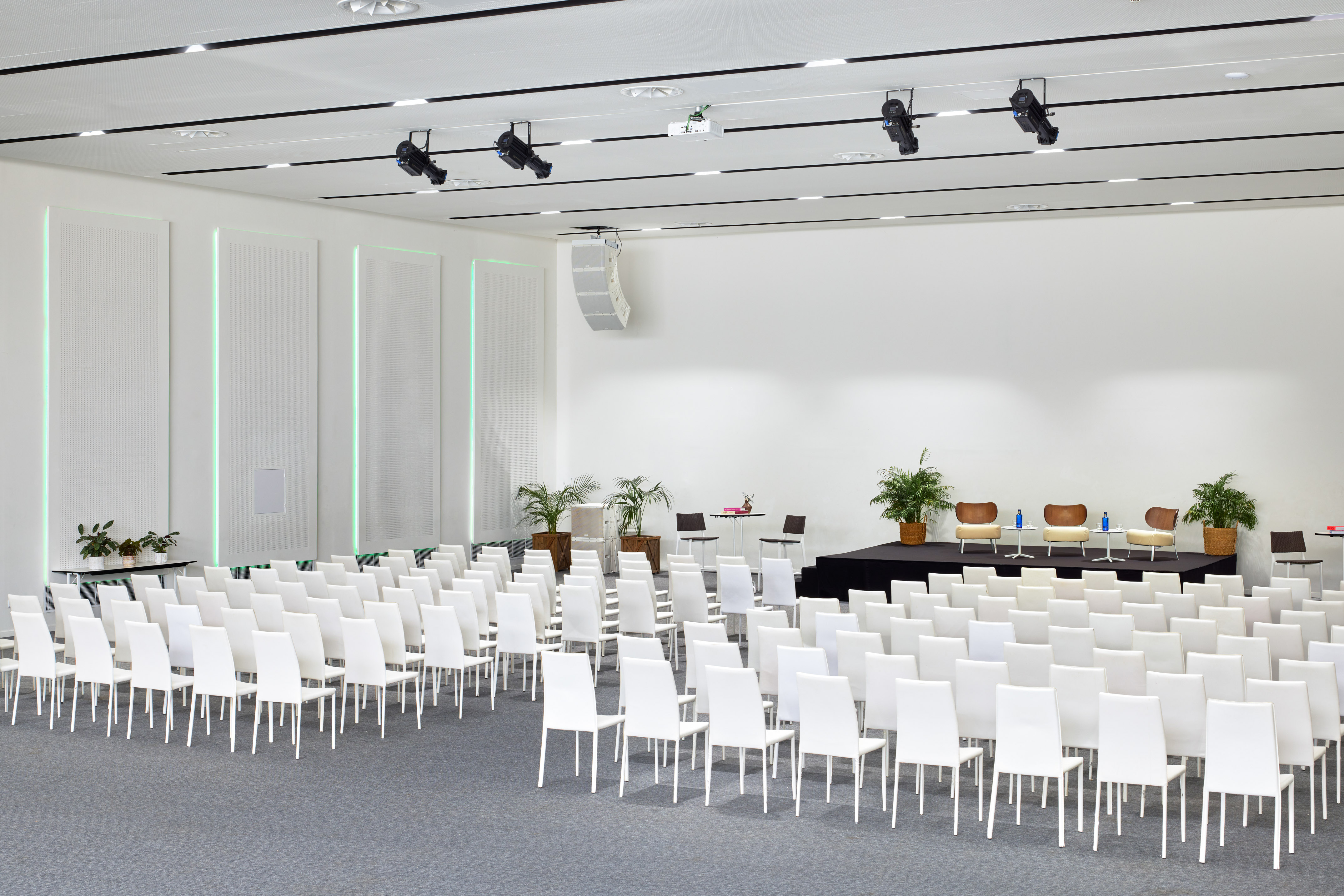 Empty modern event space with white chairs, stage, and presentation setup.