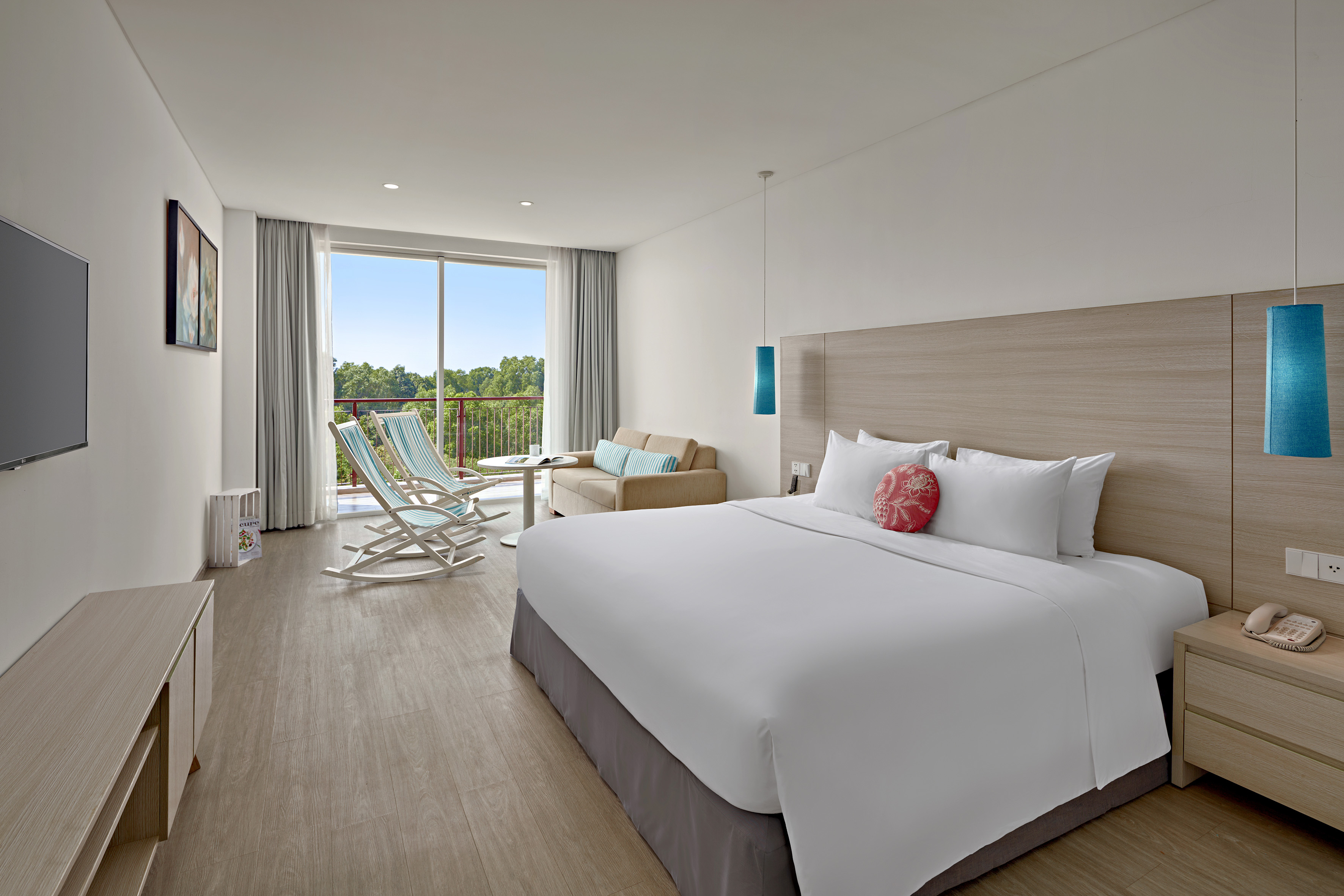 Modern hotel bedroom with king bed, balcony forest view, and lounge chairs.