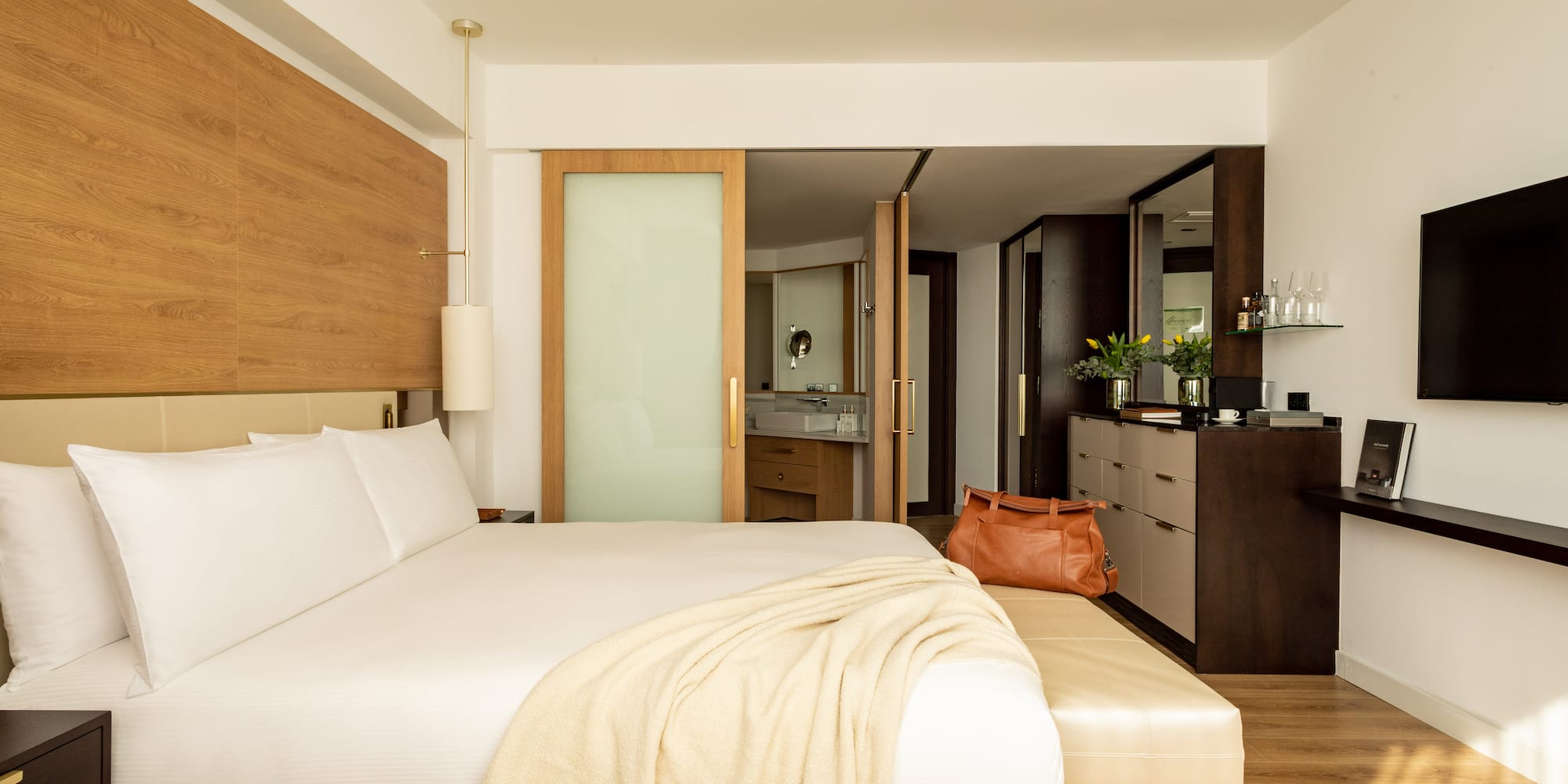 a bed with a white blanket and a brown bag in a room