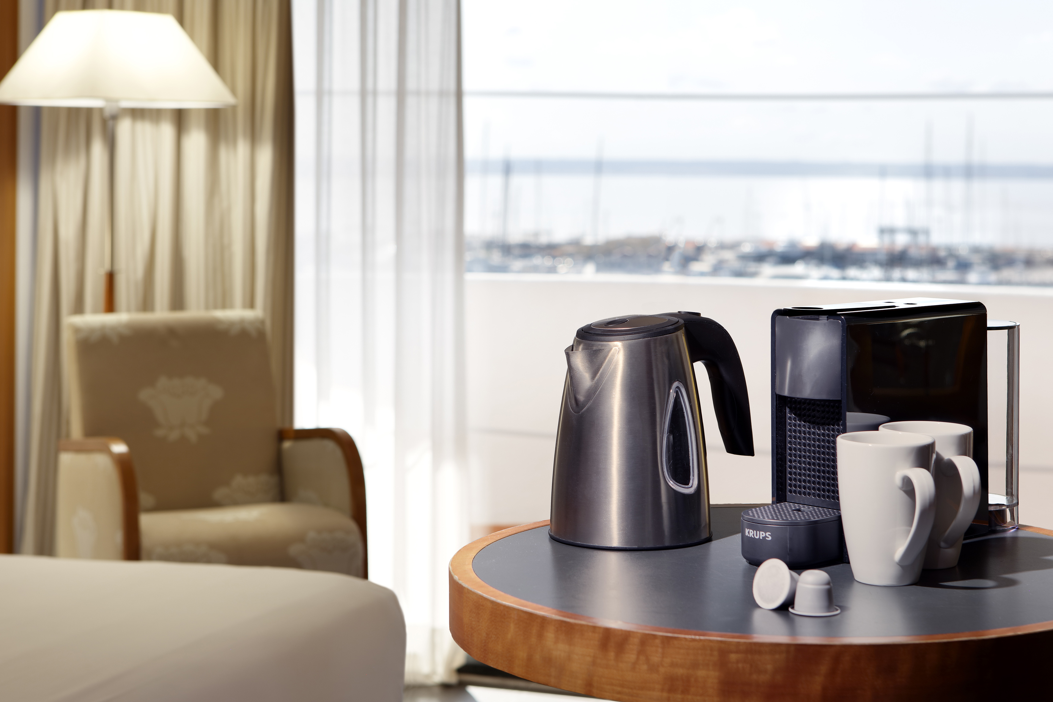 Hotel room with Krups coffee machine, kettle, mugs, and marina view.