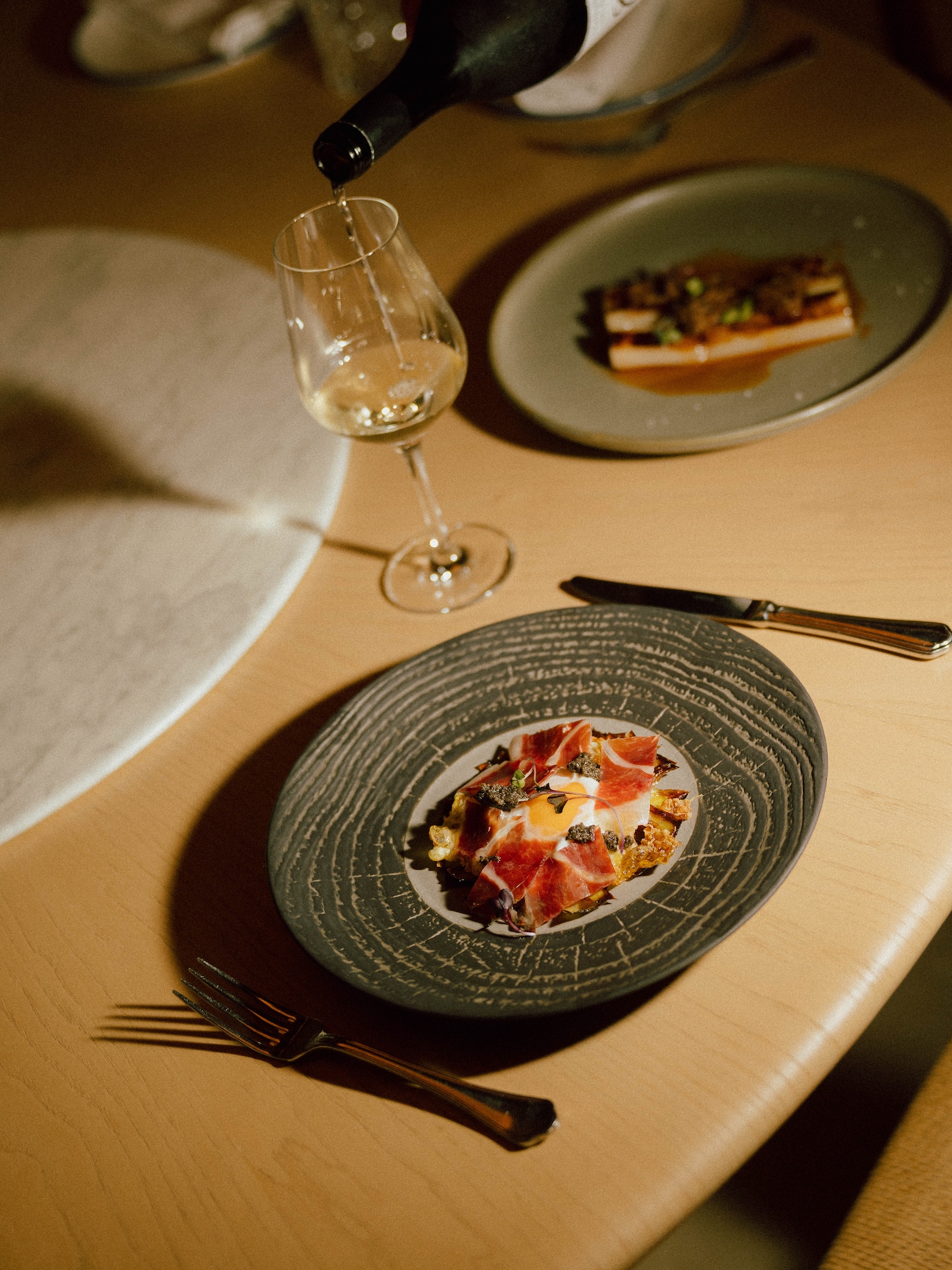 Pouring white wine; plate of Iberian ham, fried egg, and truffle.
